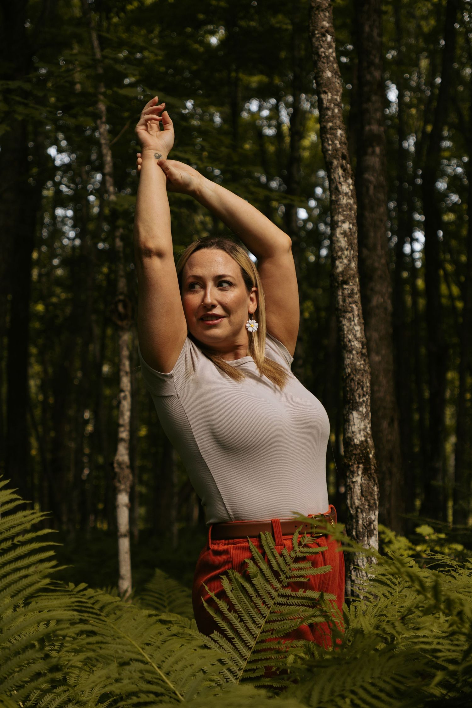 Person in white top and patterned skirt poses among ferns in a forest setting.