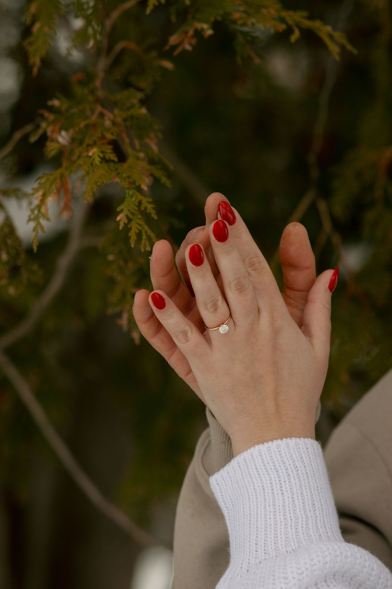 Close-up of hands with red nail polish and white sweater sleeves against an autumn background.