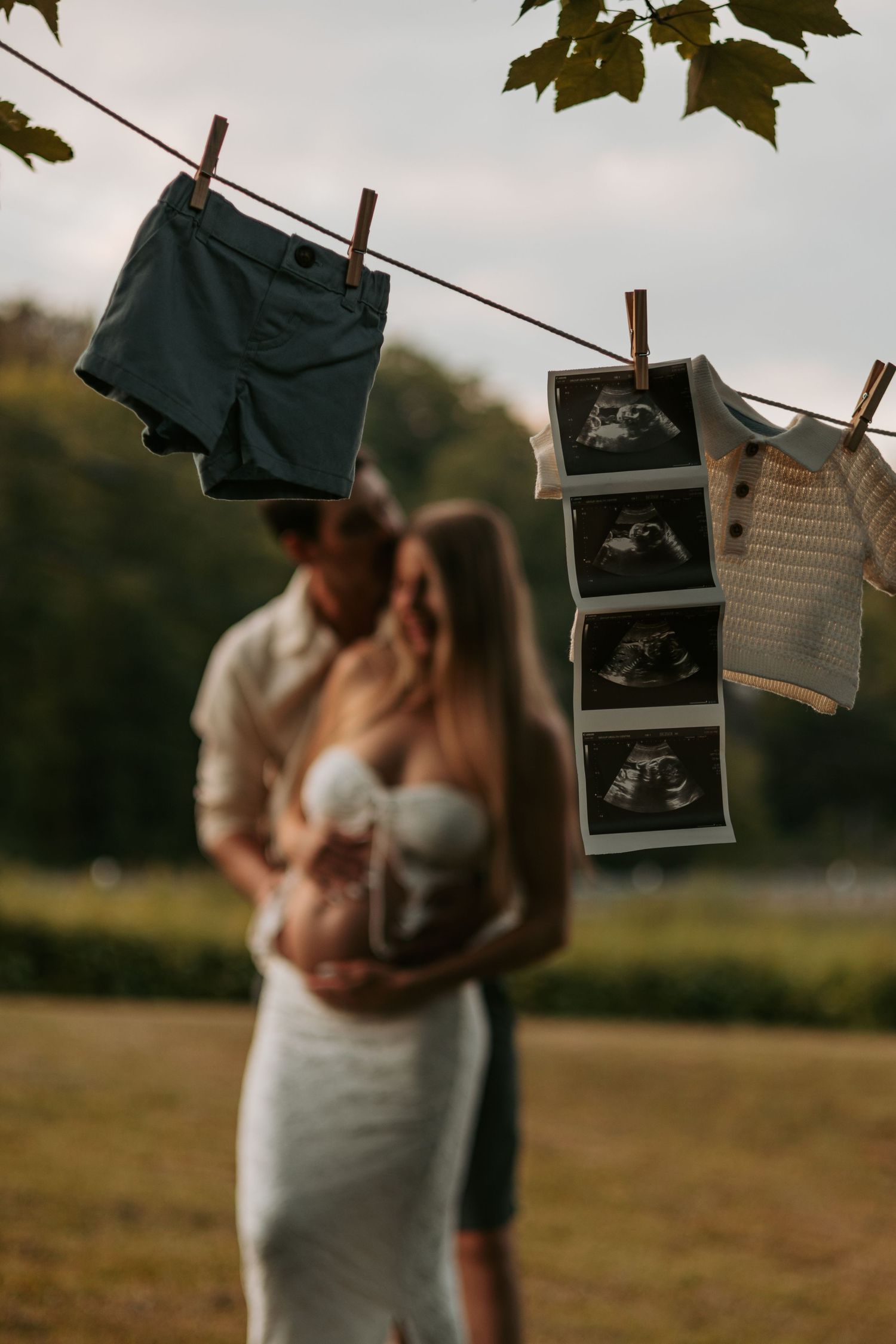 Baby announcement scene with ultrasound photos hanging on clothesline at sunset.