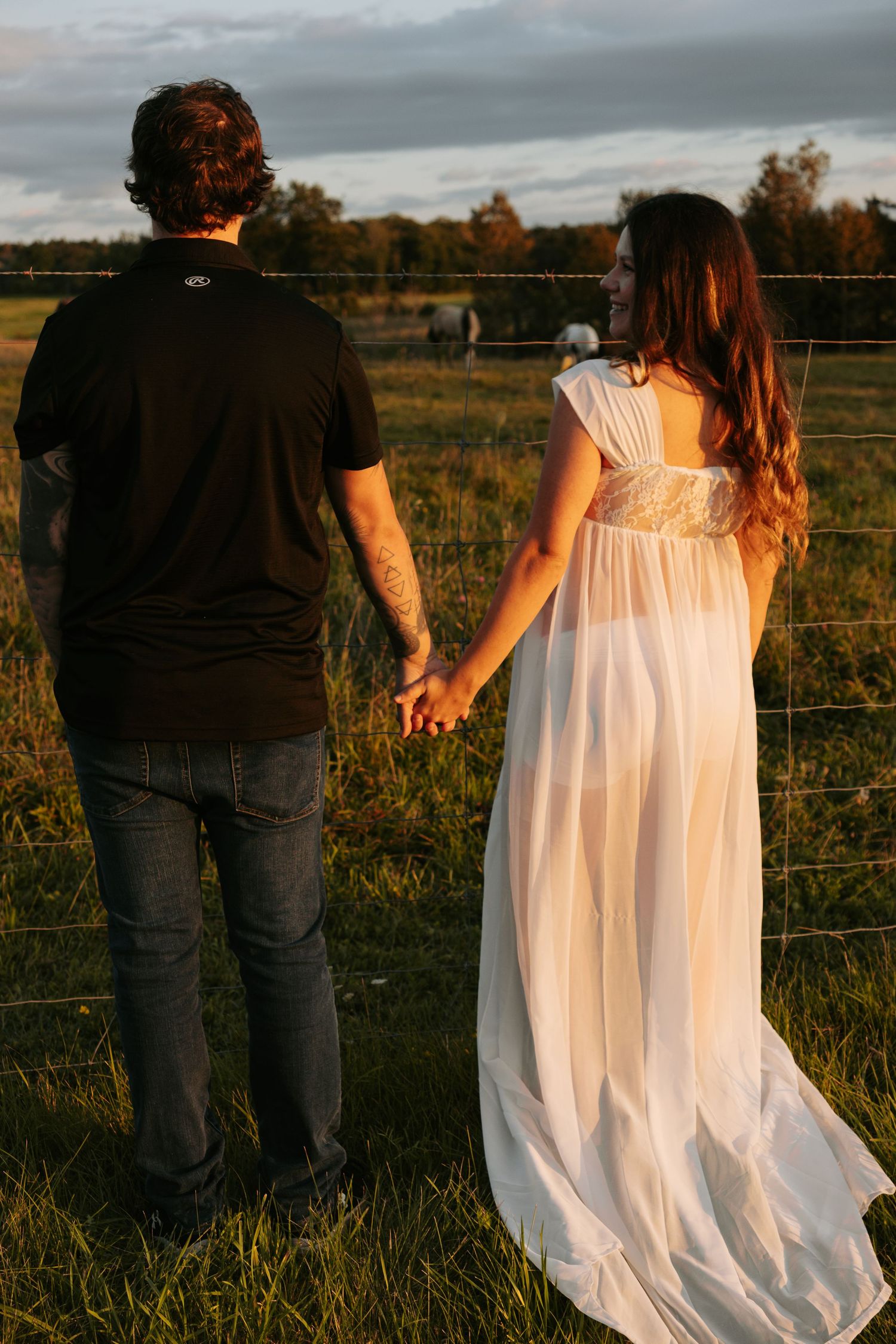 Back view of couple walking along fence line in rural field during evening light.