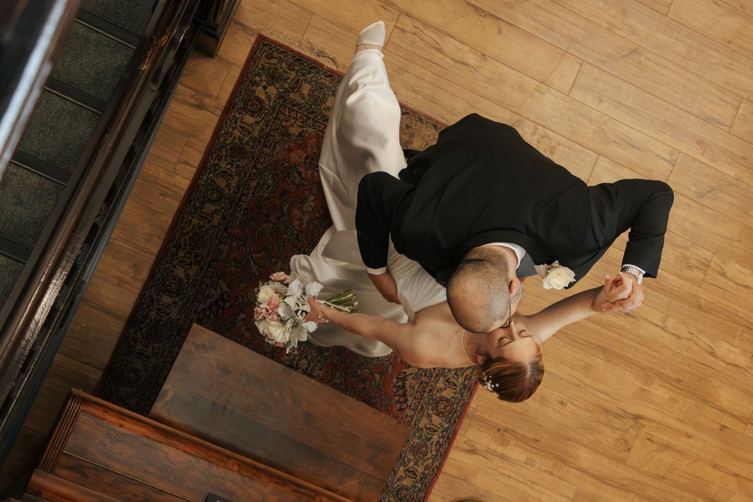 Aerial view of bride and groom sharing a romantic dip dance on hardwood floor during wedding reception.