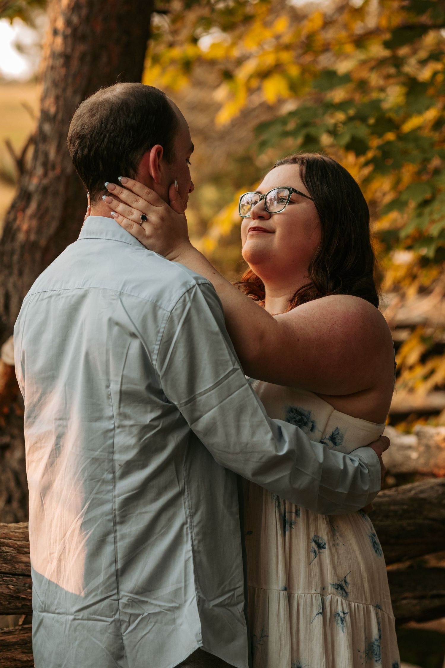Couple embraces tenderly against autumn foliage background.