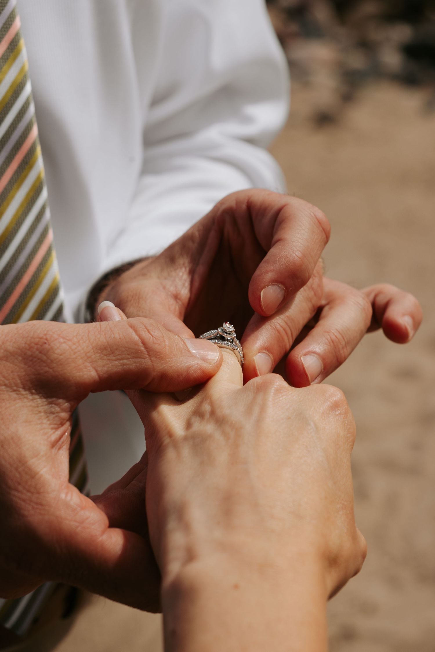 Close-up of hands exchanging rings during a wedding ceremony on the beach.