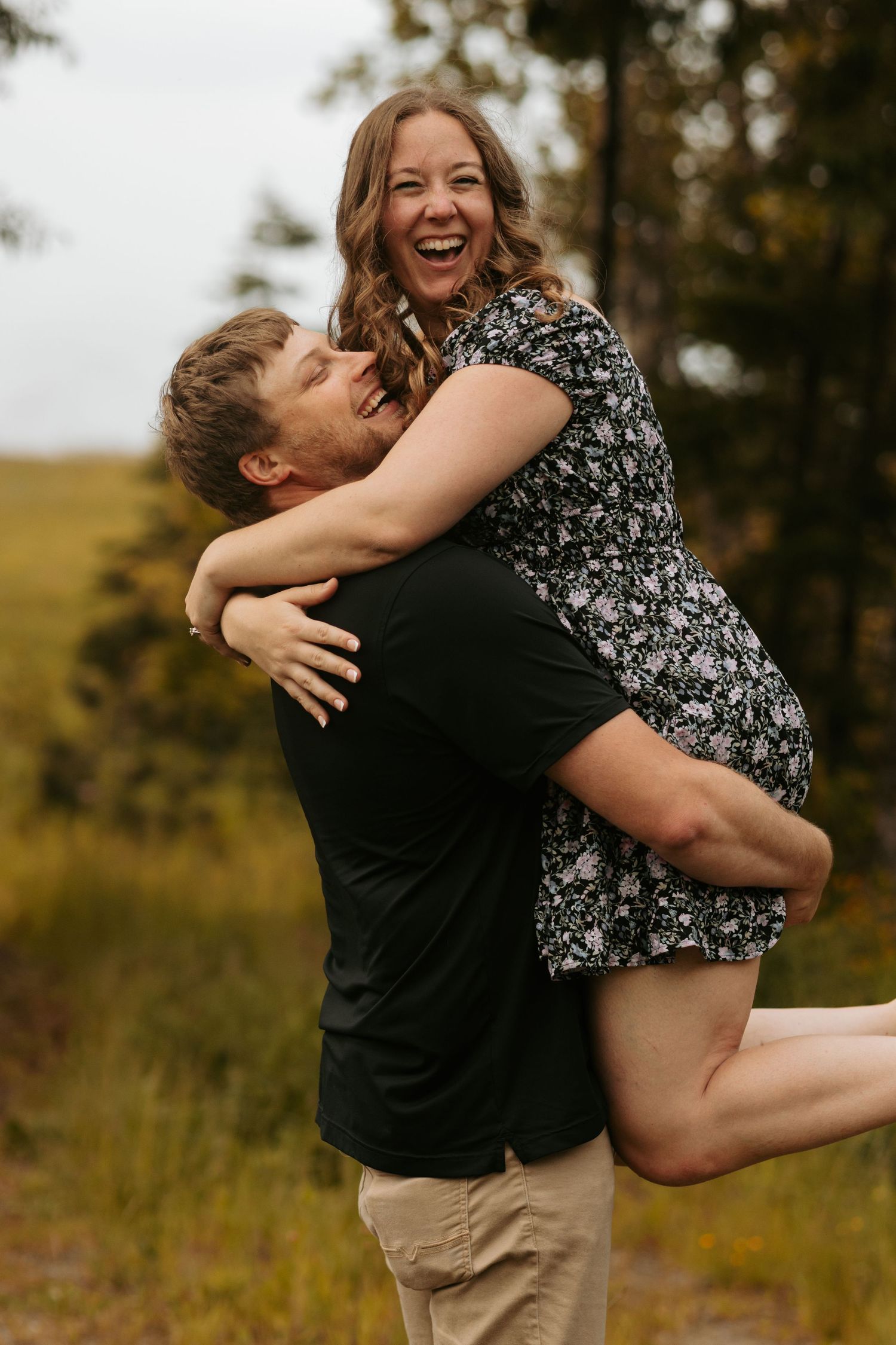 Playful couple embracing and spinning in a grassy field during sunset.