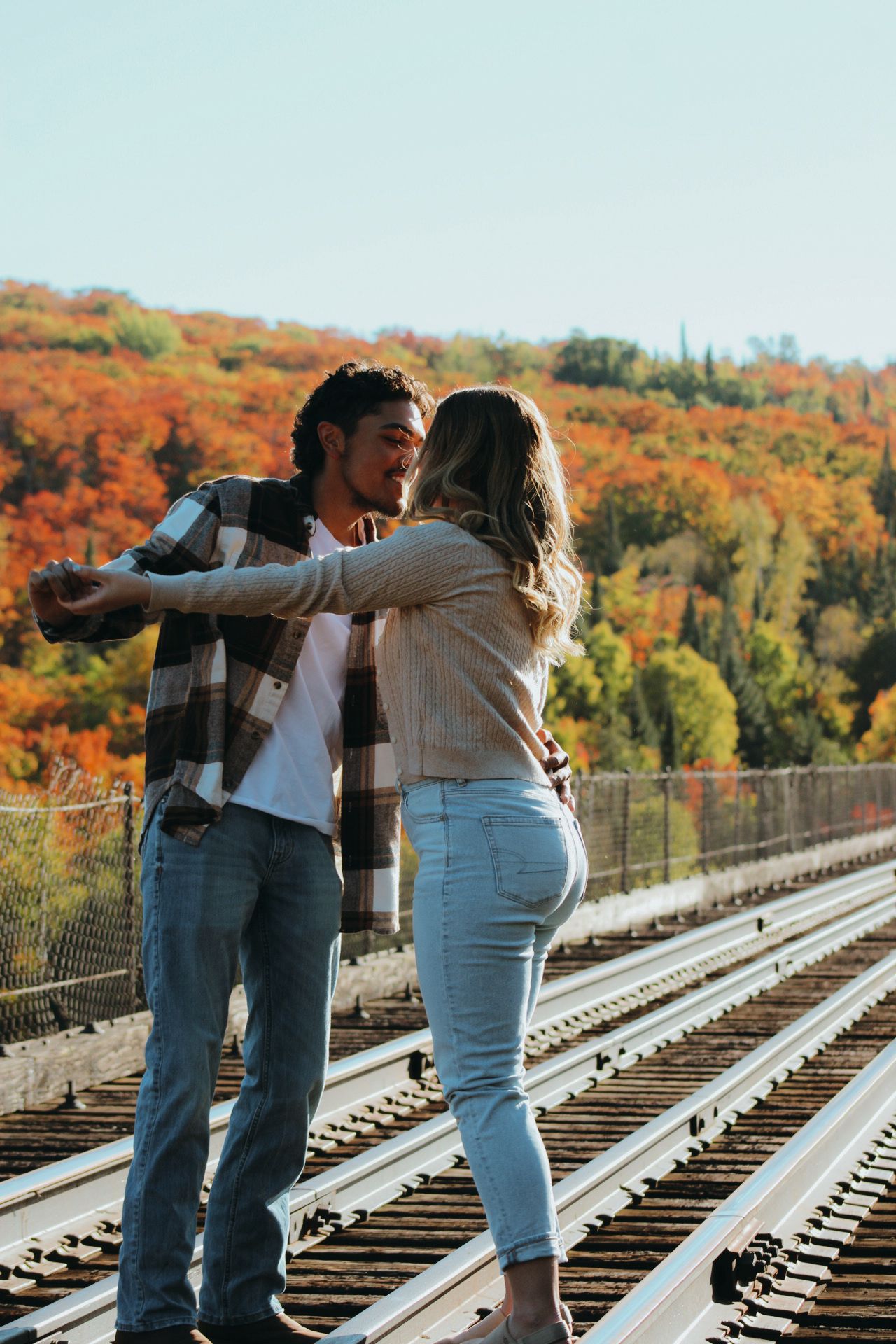 Two people share a romantic dance on train tracks with fall colors in the background.