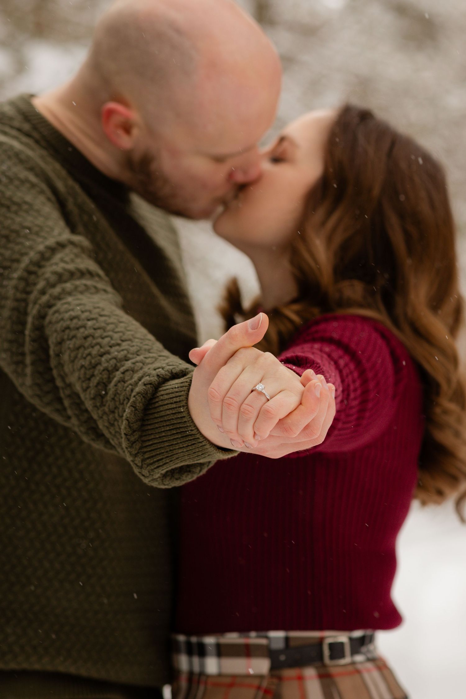 A romantic winter engagement photo showing a close-up of a couple embracing in cozy sweaters.