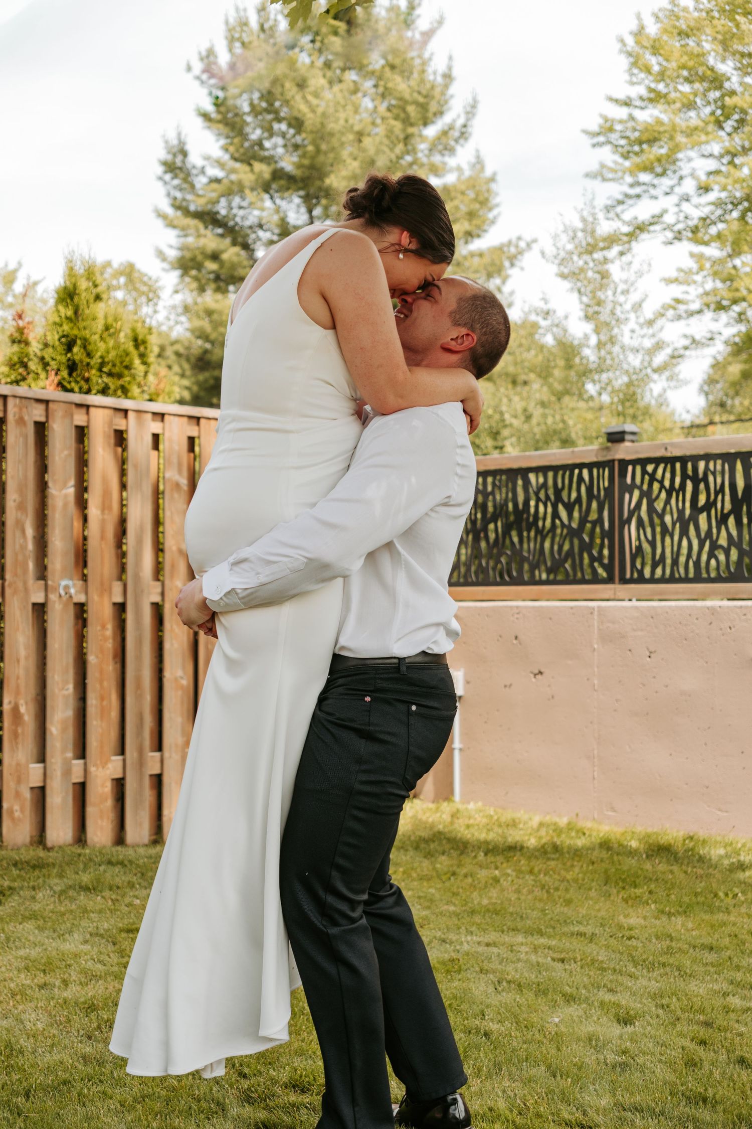 Newlyweds share an intimate embrace in front of a rustic wooden fence during their wedding celebration.