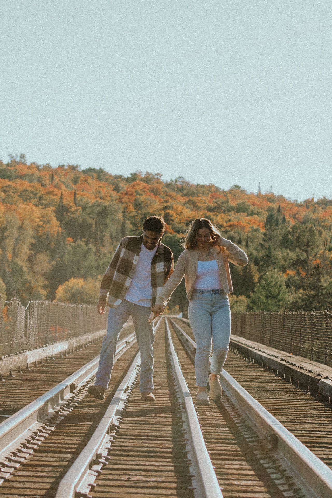 Two people walk hand in hand along railroad tracks during golden autumn.
