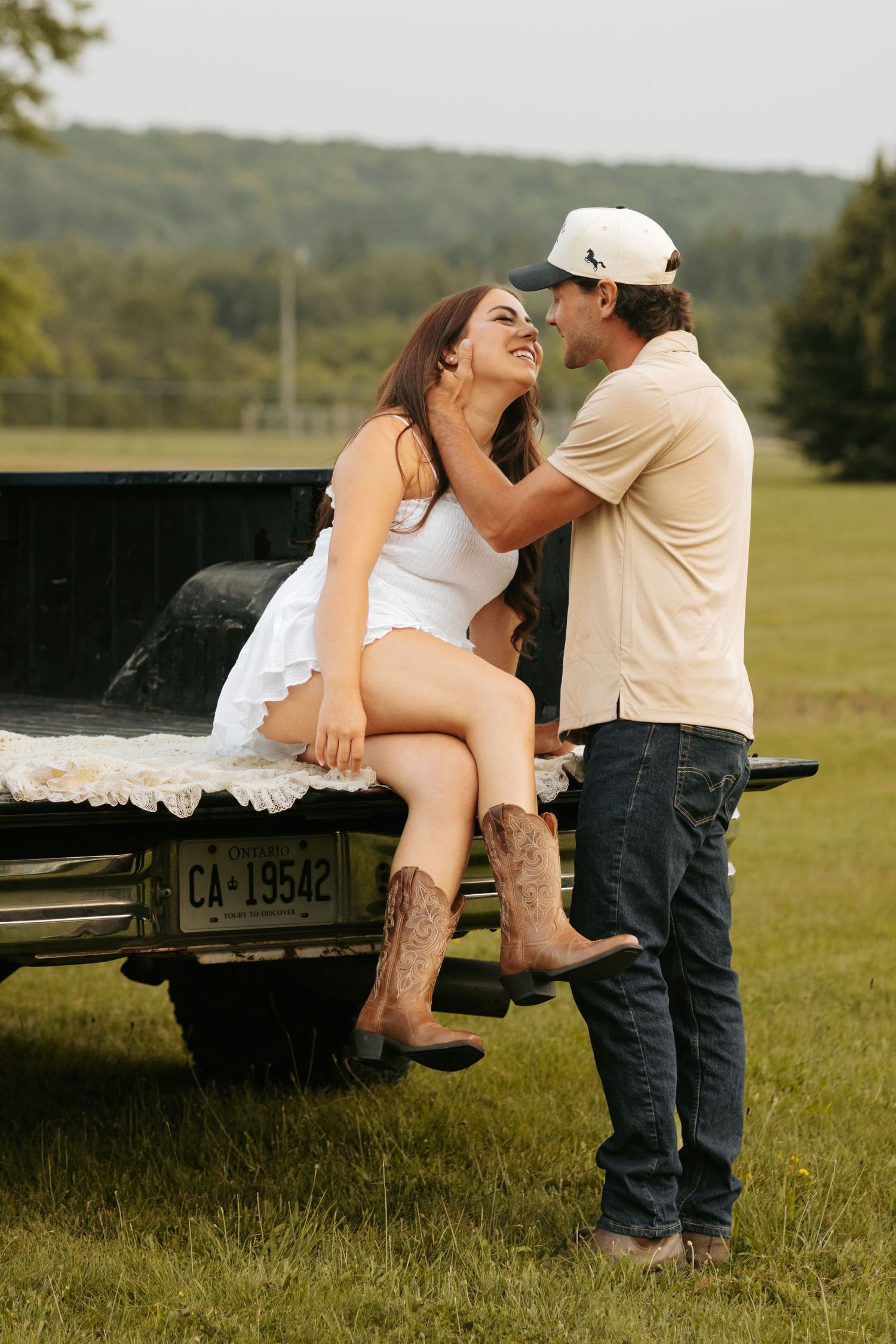Couple in casual attire posing playfully on pickup truck tailgate in rural setting.