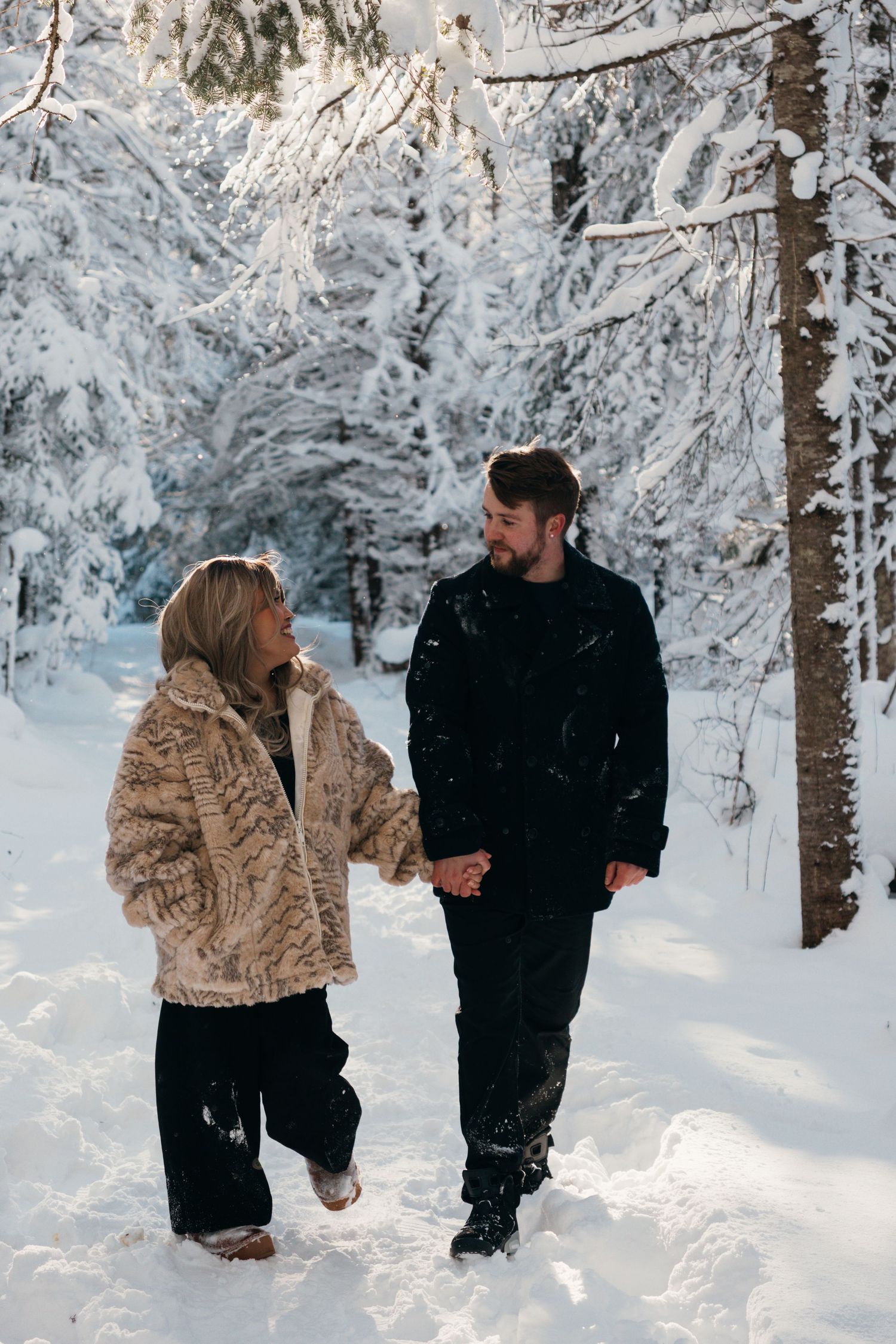 A couple walks hand in hand through a magical snow-covered winter forest.