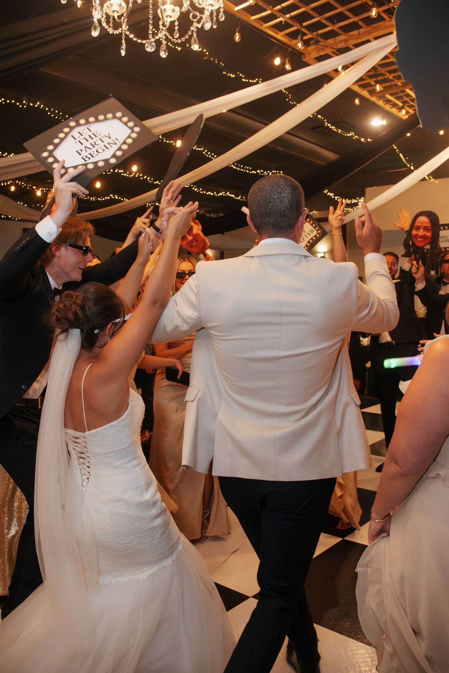 Bride and groom dancing with guests at elegant wedding reception with string lights and flowing ribbons.