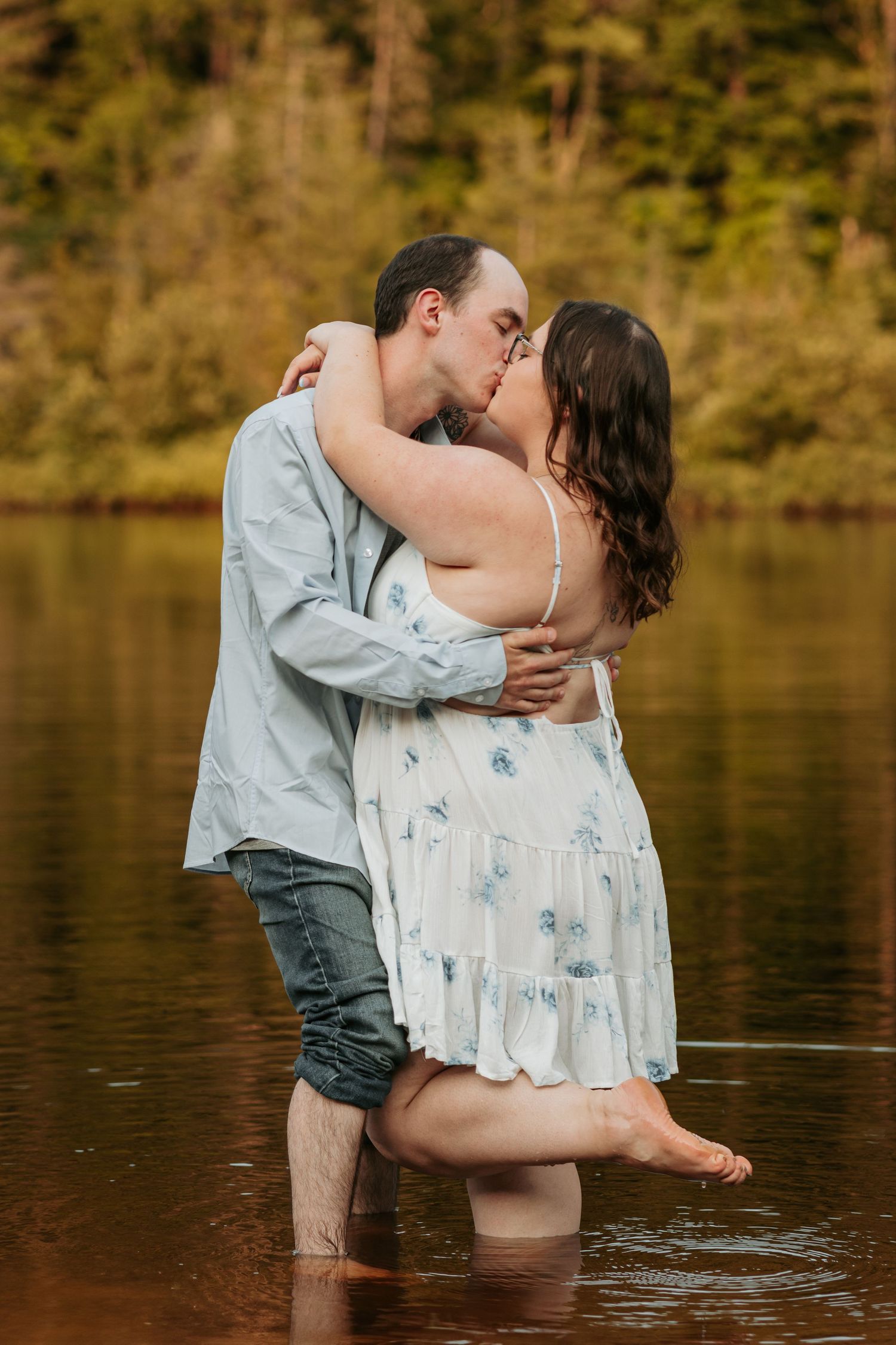 Romantic couple embraces while standing in lake water during sunset.