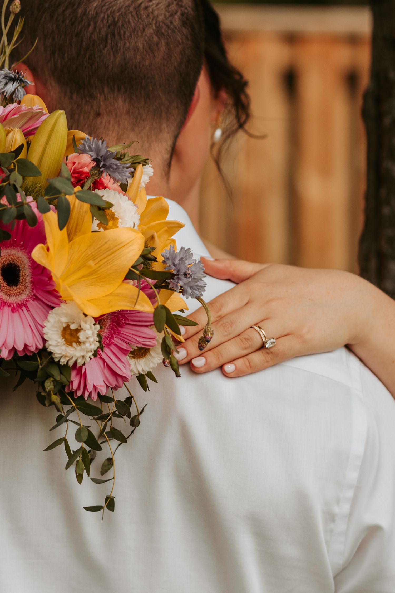 A colorful wedding bouquet with yellow lilies and pink gerbera daisies rests against a white dress.
