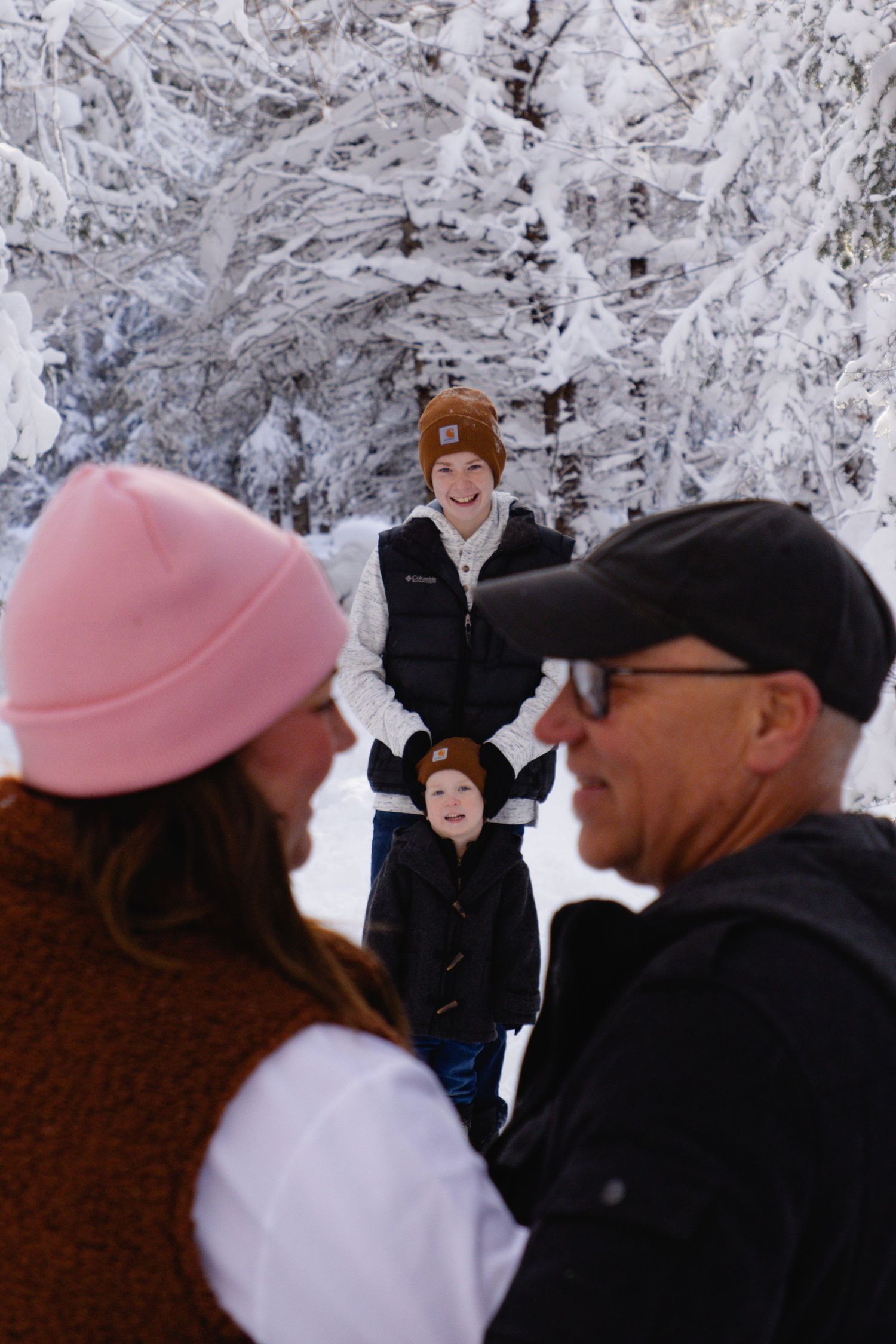 A group shares joyful reactions during a winter proposal in a snow-covered forest.