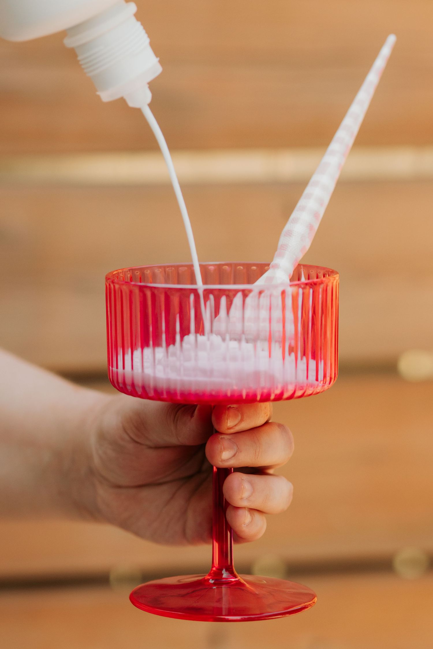 Hands pouring white liquid into a red plastic container in sequence.