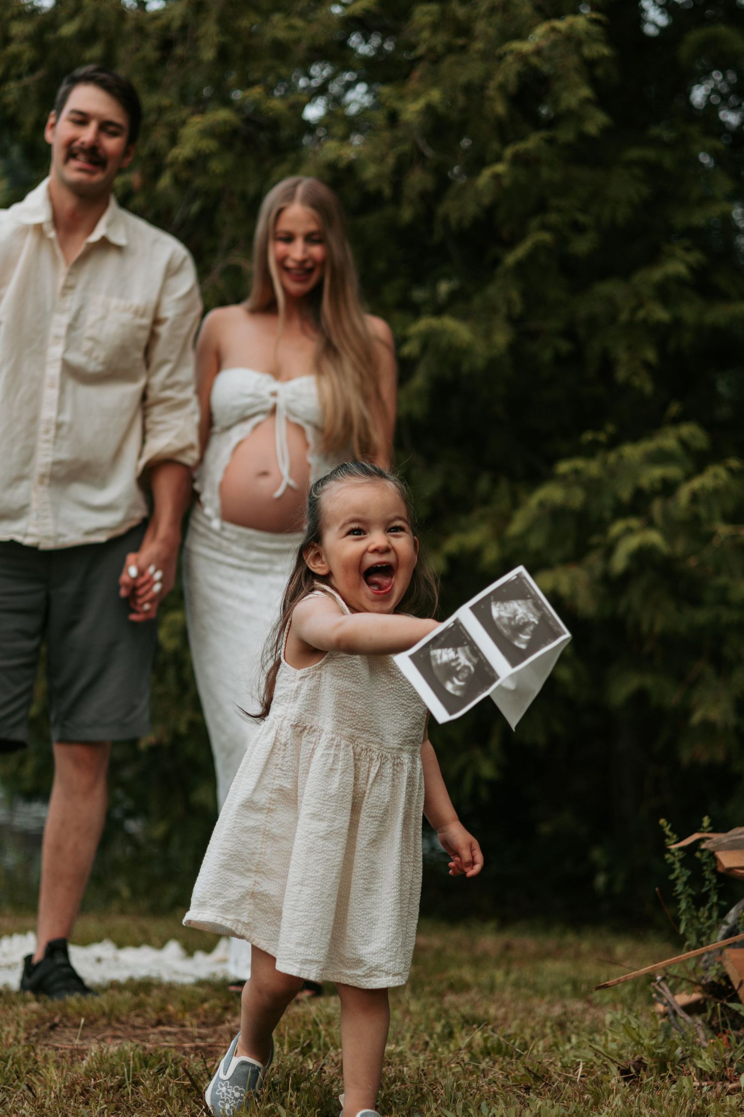 Family celebrating pregnancy announcement outdoors with ultrasound photos and joyful expressions.
