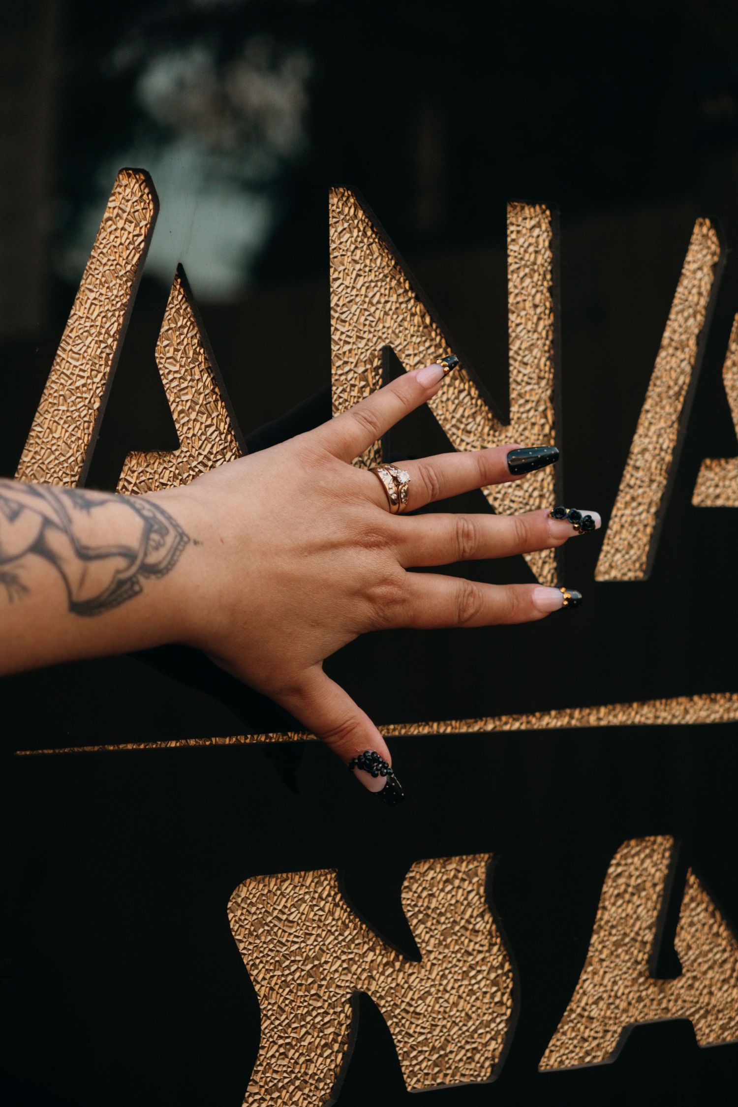 Artistic shot of a tattooed hand reaching across textured golden light and shadows.