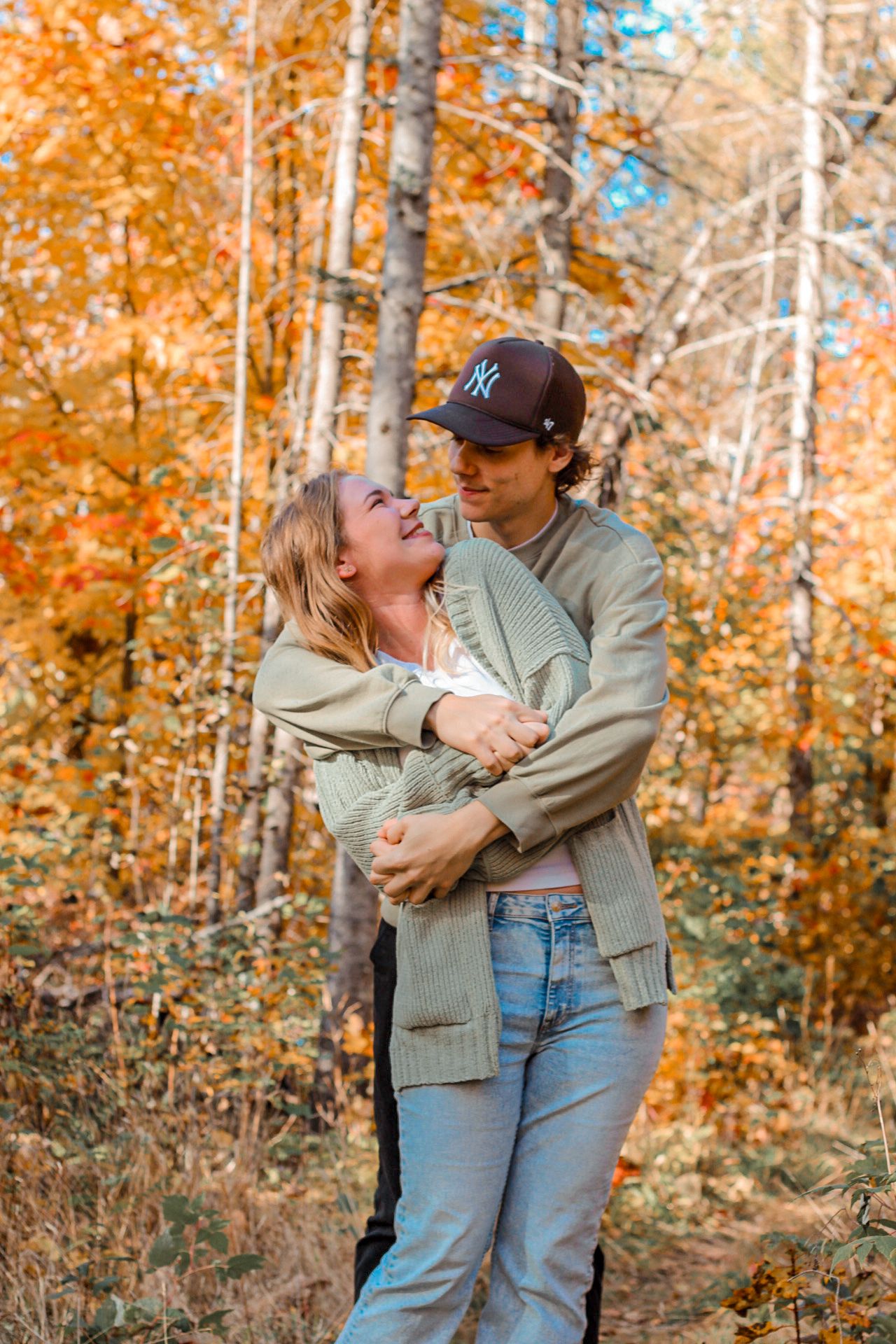 A couple shares a playful moment in autumn woods with vibrant orange foliage.