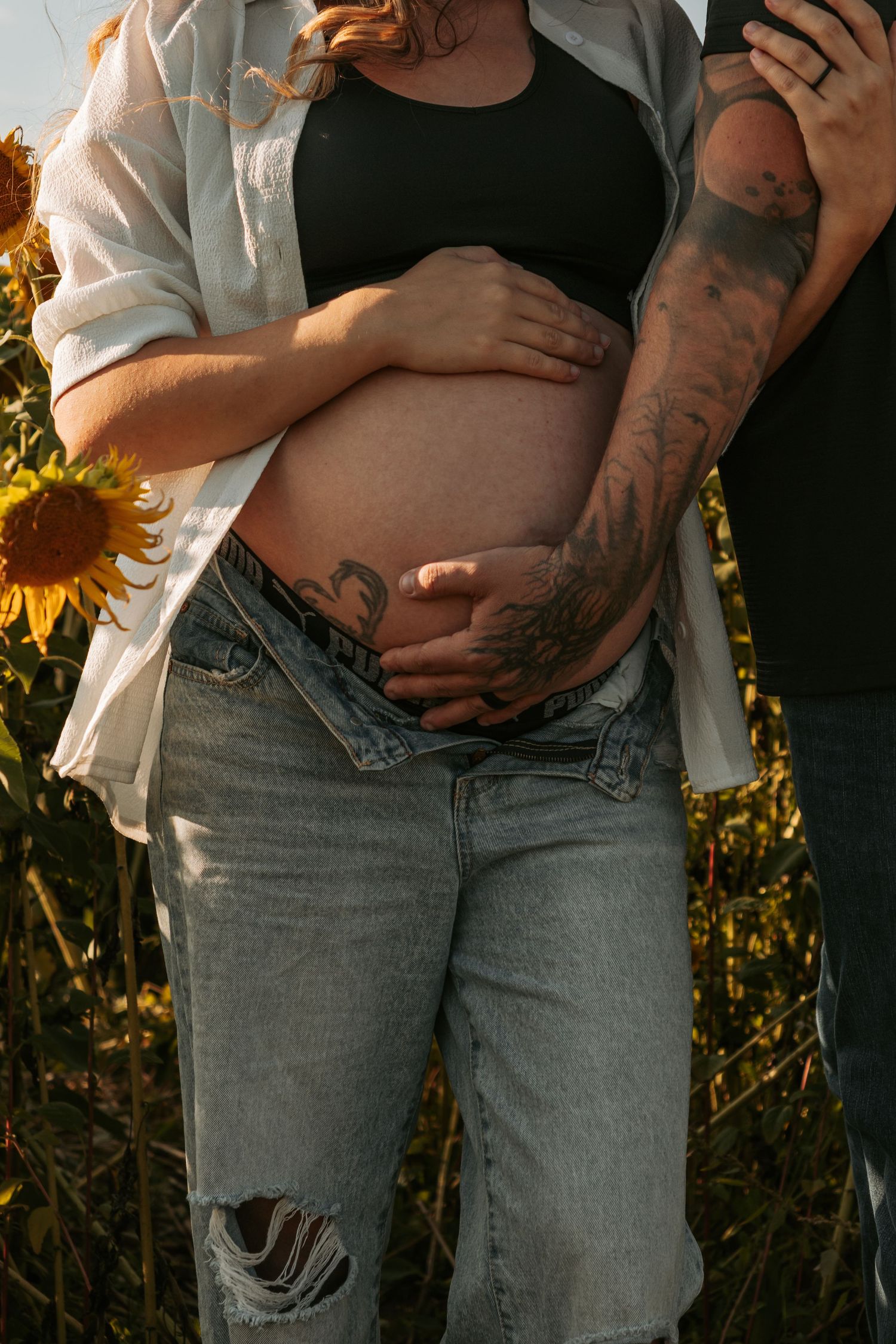 A couple embraces in a sunflower field during golden hour, showing an intimate pregnancy announcement moment.