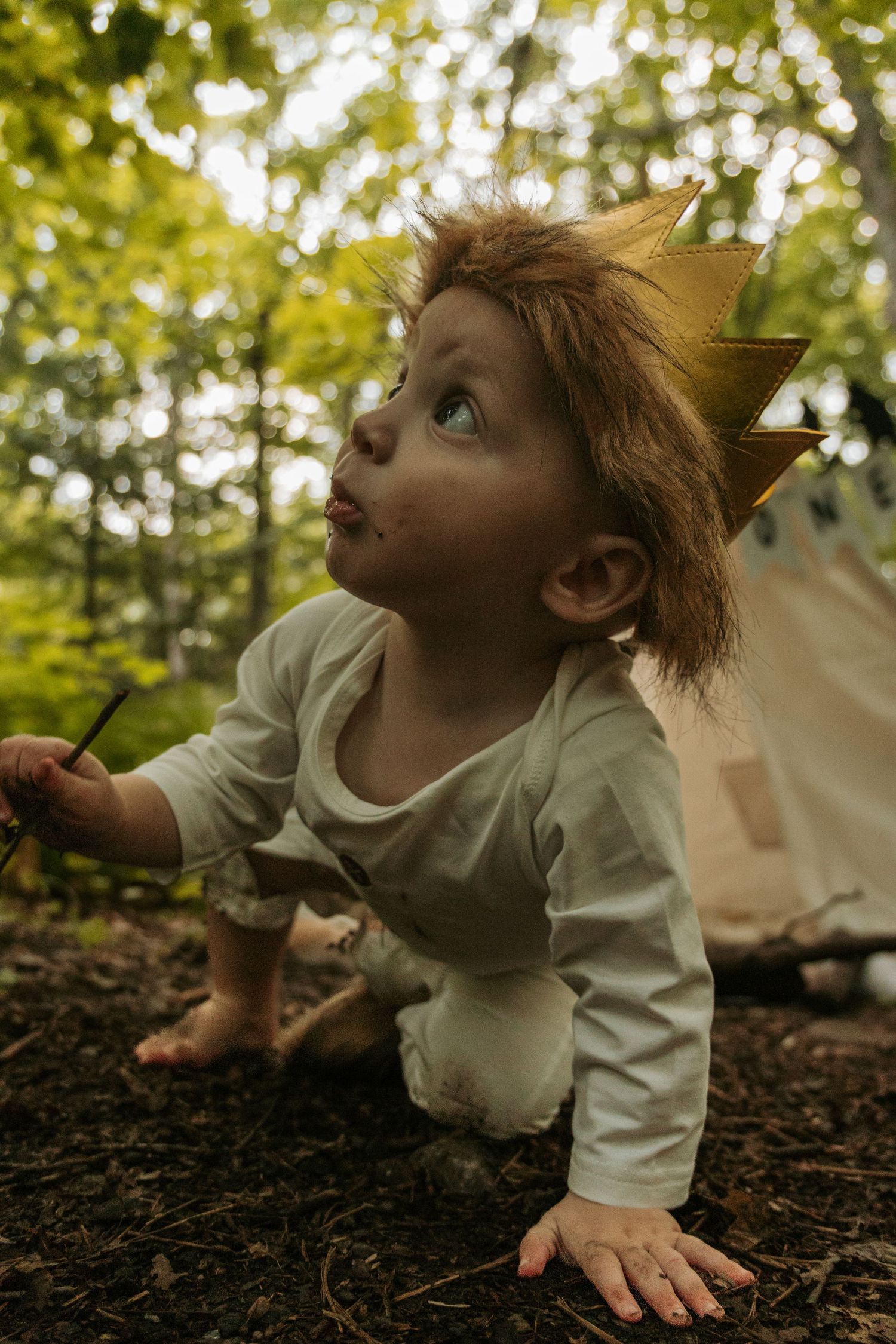 Young child in light colored outfit playing near teepee tent outdoors.