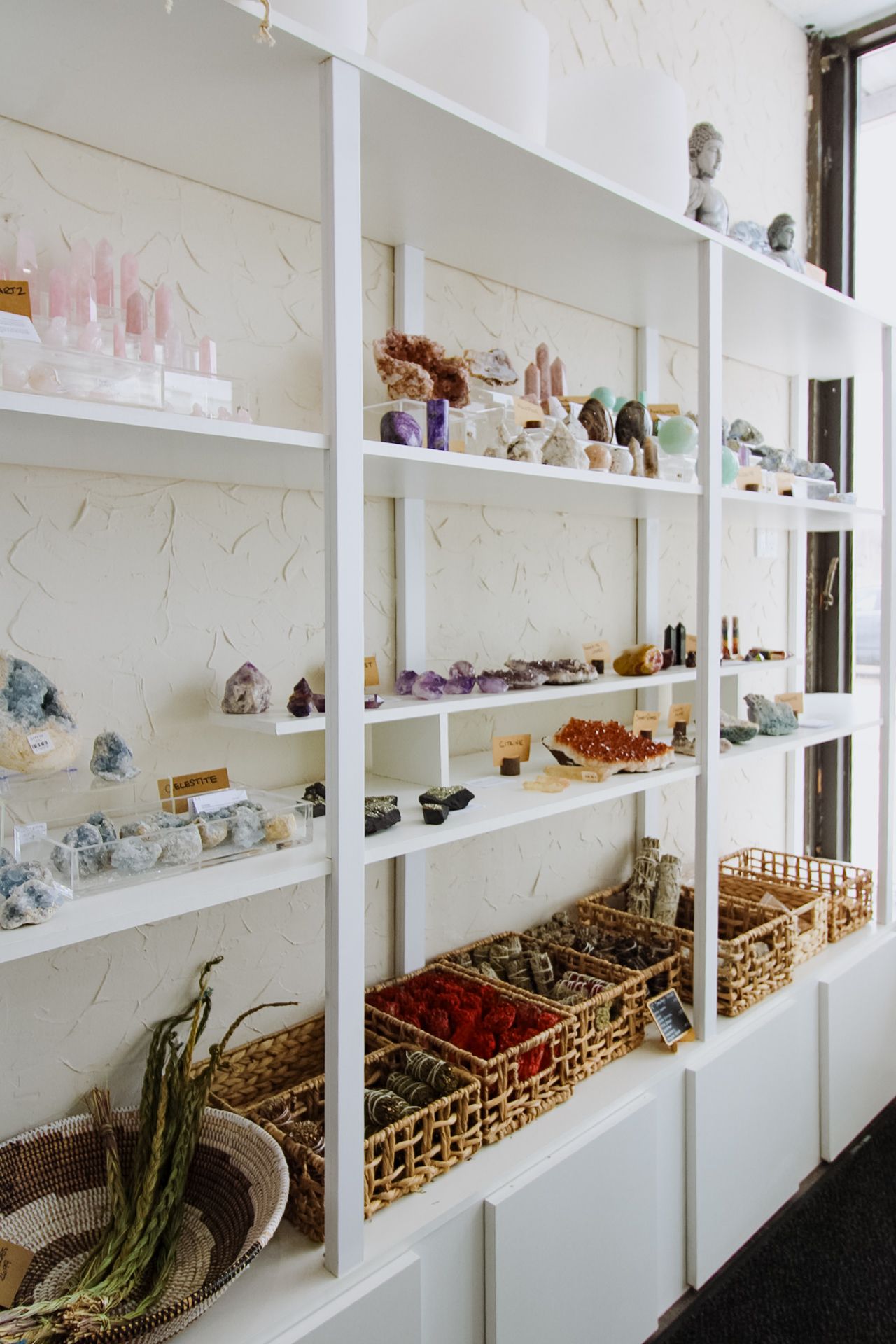 White shelving units lined with crystals, minerals and decorative items in a bright retail space.