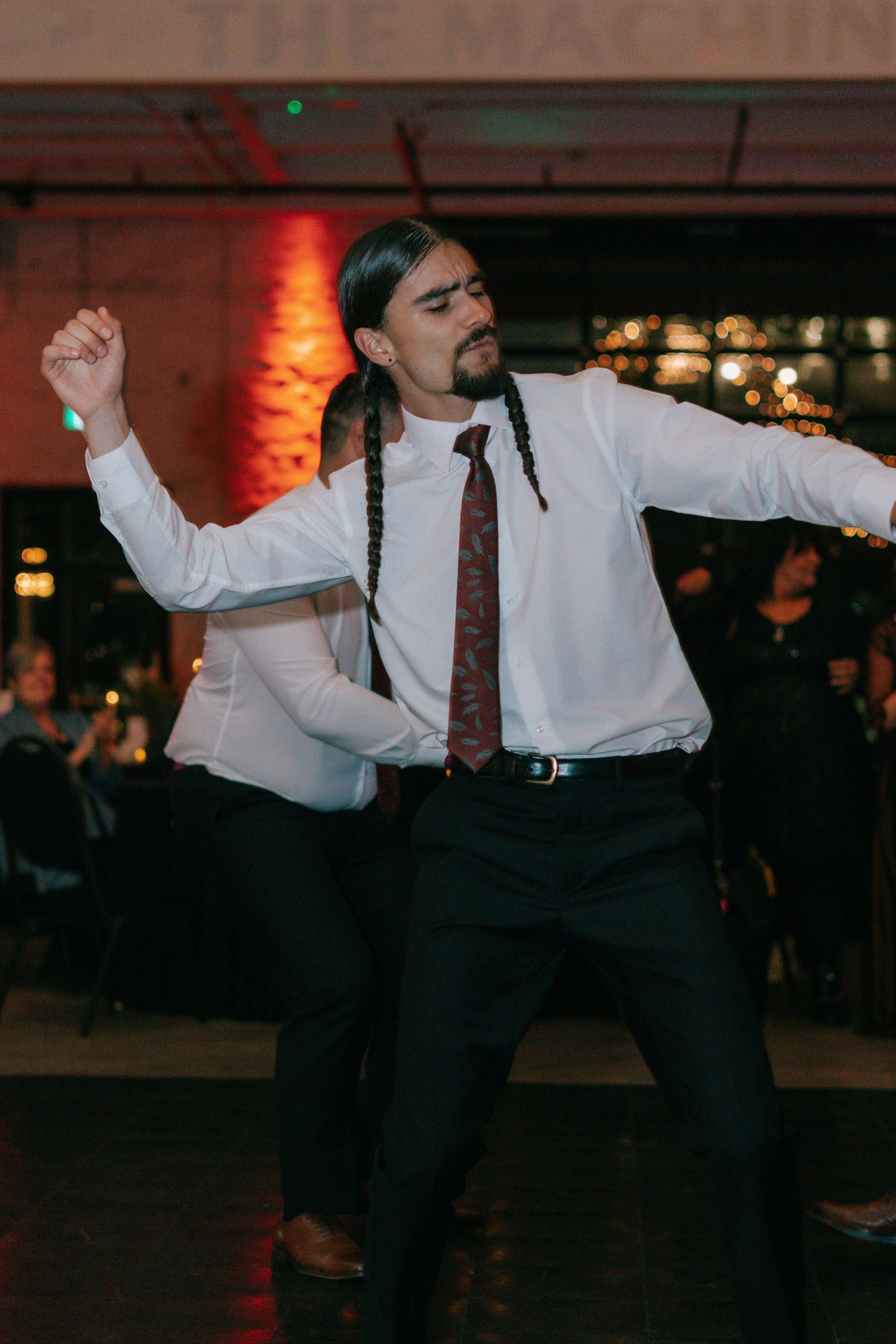 A guest shows off dramatic dance moves at a wedding reception with red-lit brick walls.