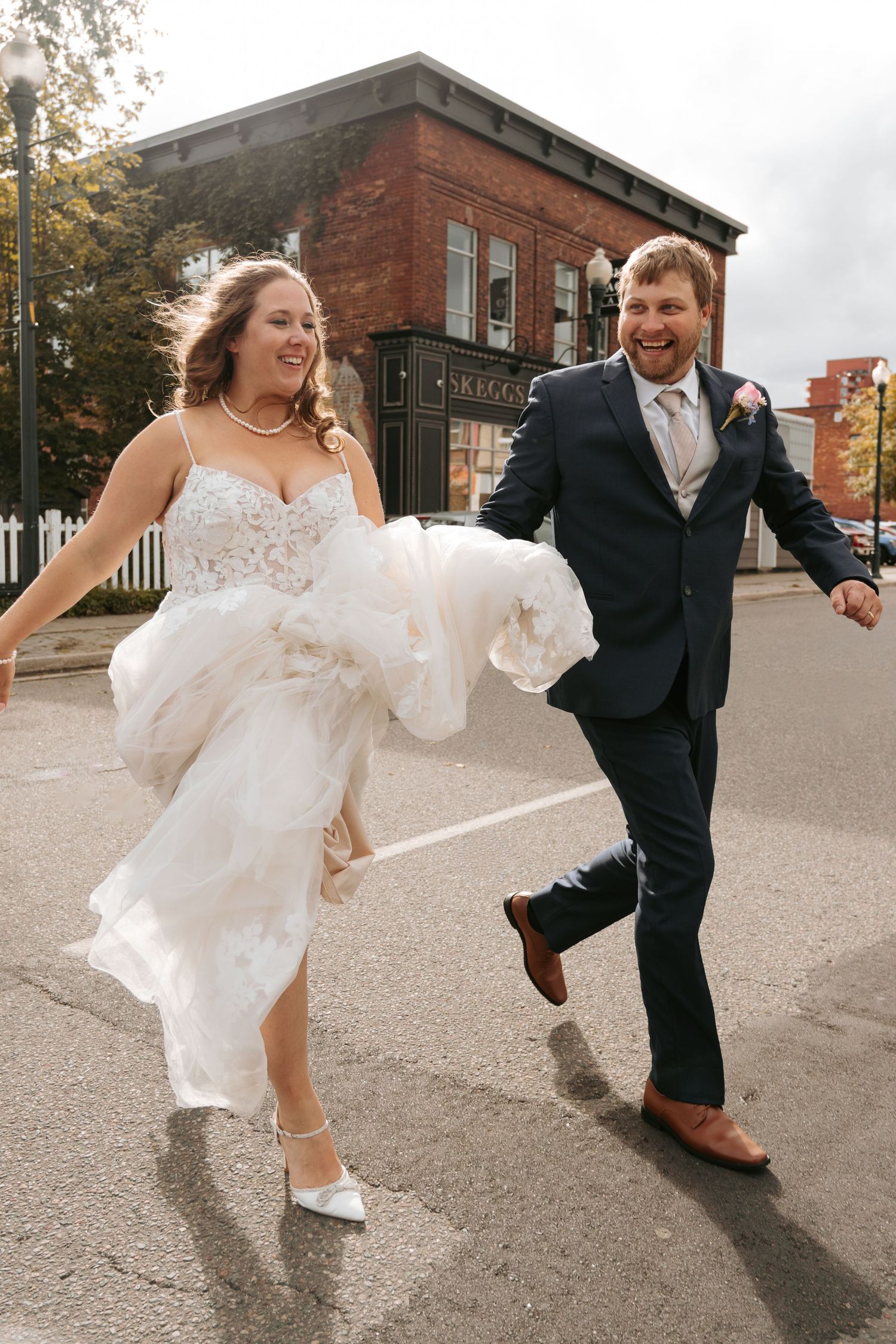 Playful wedding couple dances and spins on a pathway near historic buildings.