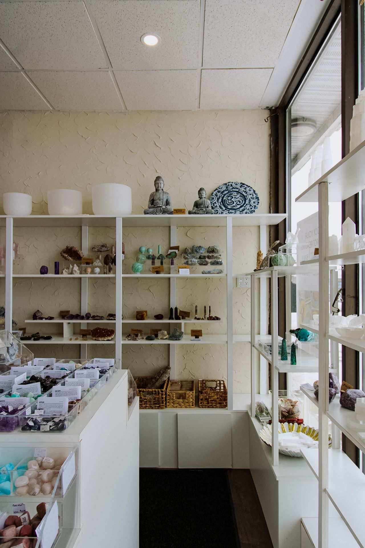 Interior view of a crystal shop with white shelving units displaying minerals and spiritual items.