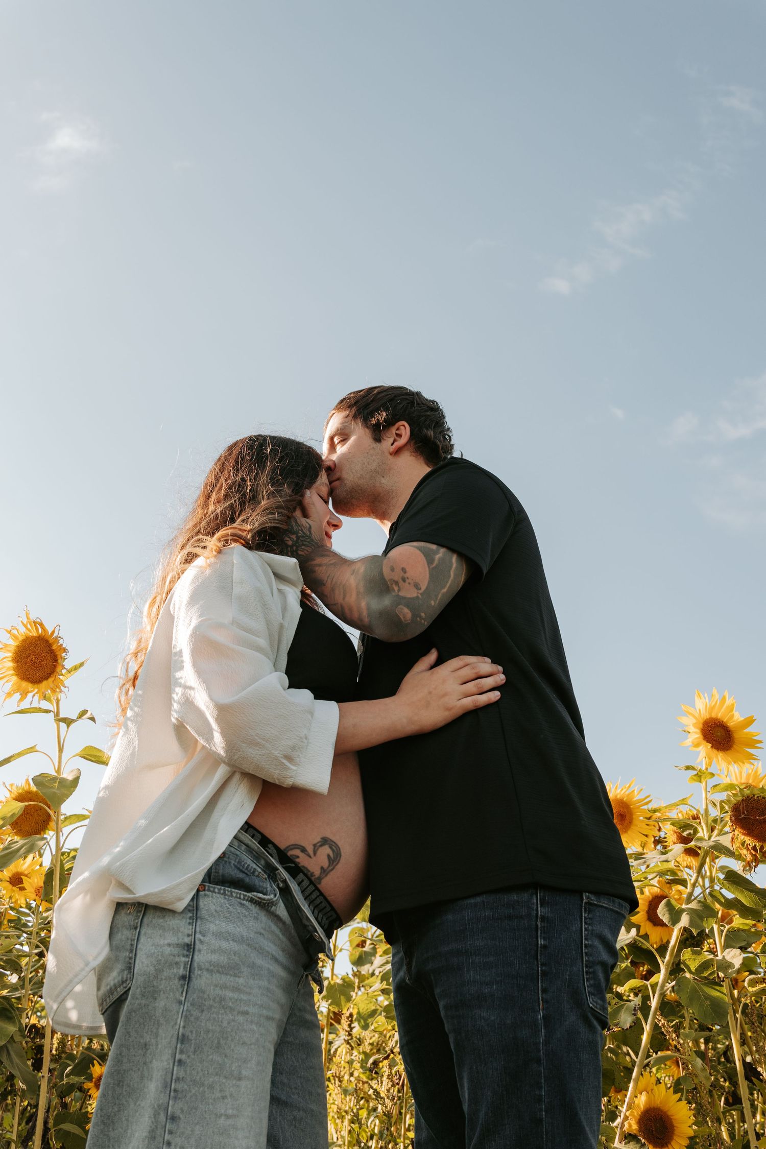 Romantic couple sharing intimate moment in sunflower field during sunset photoshoot.