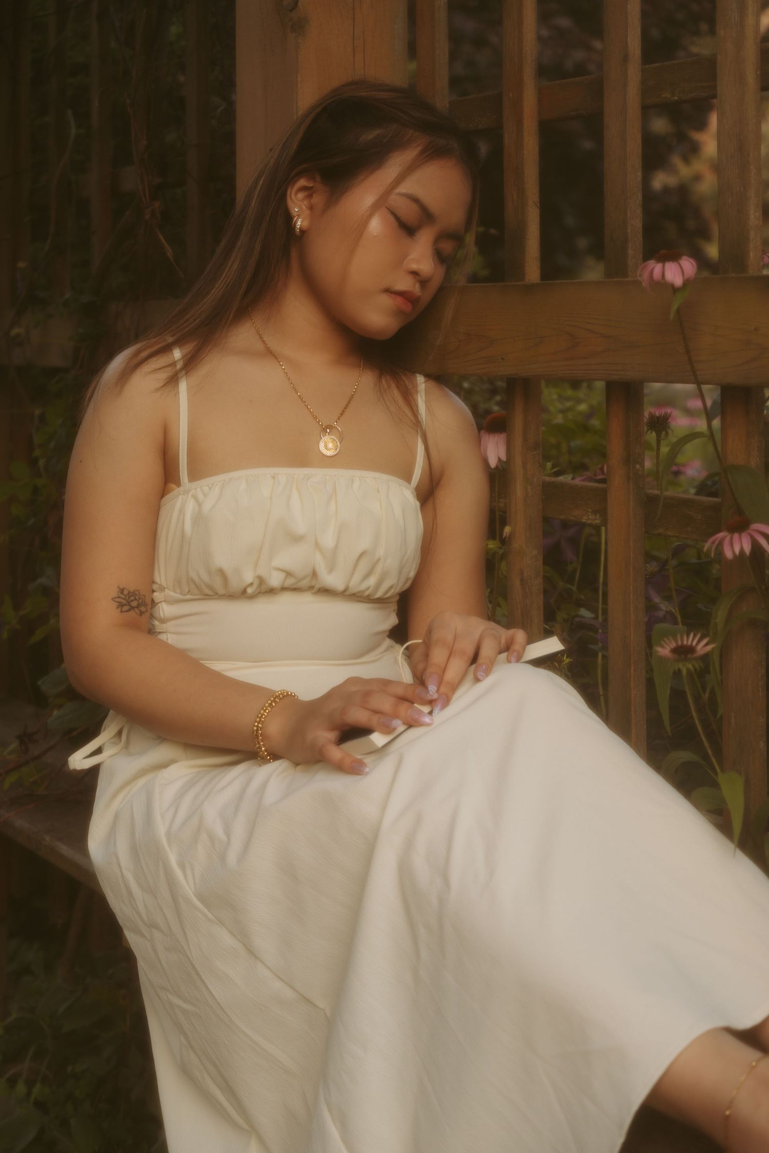 An ethereal photo of someone reading peacefully on a garden bench in a white summer dress.