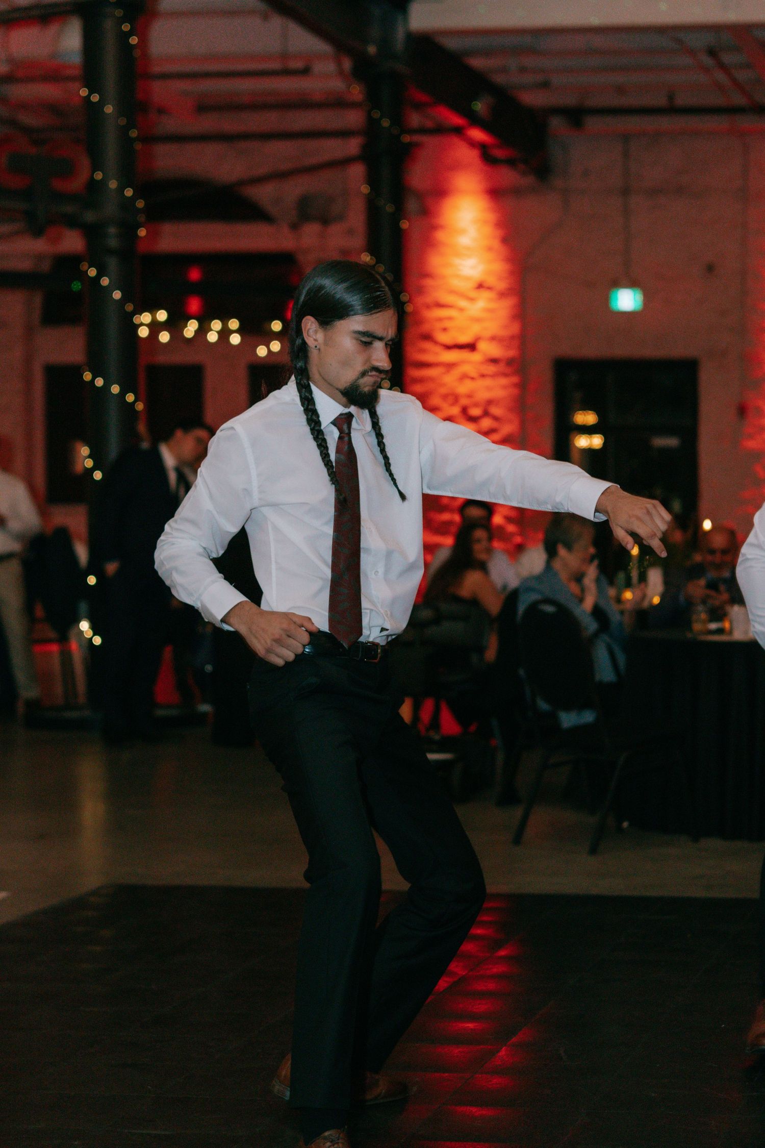 A wedding guest performs an enthusiastic solo dance in formal attire at the reception.