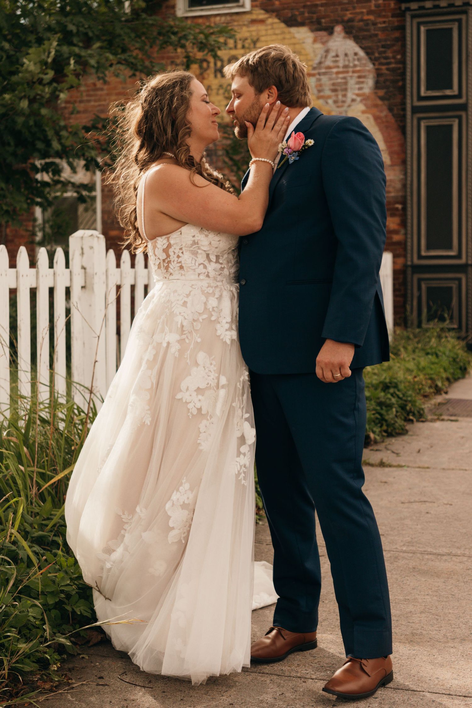 A romantic wedding moment captured against a rustic brick wall and white picket fence.