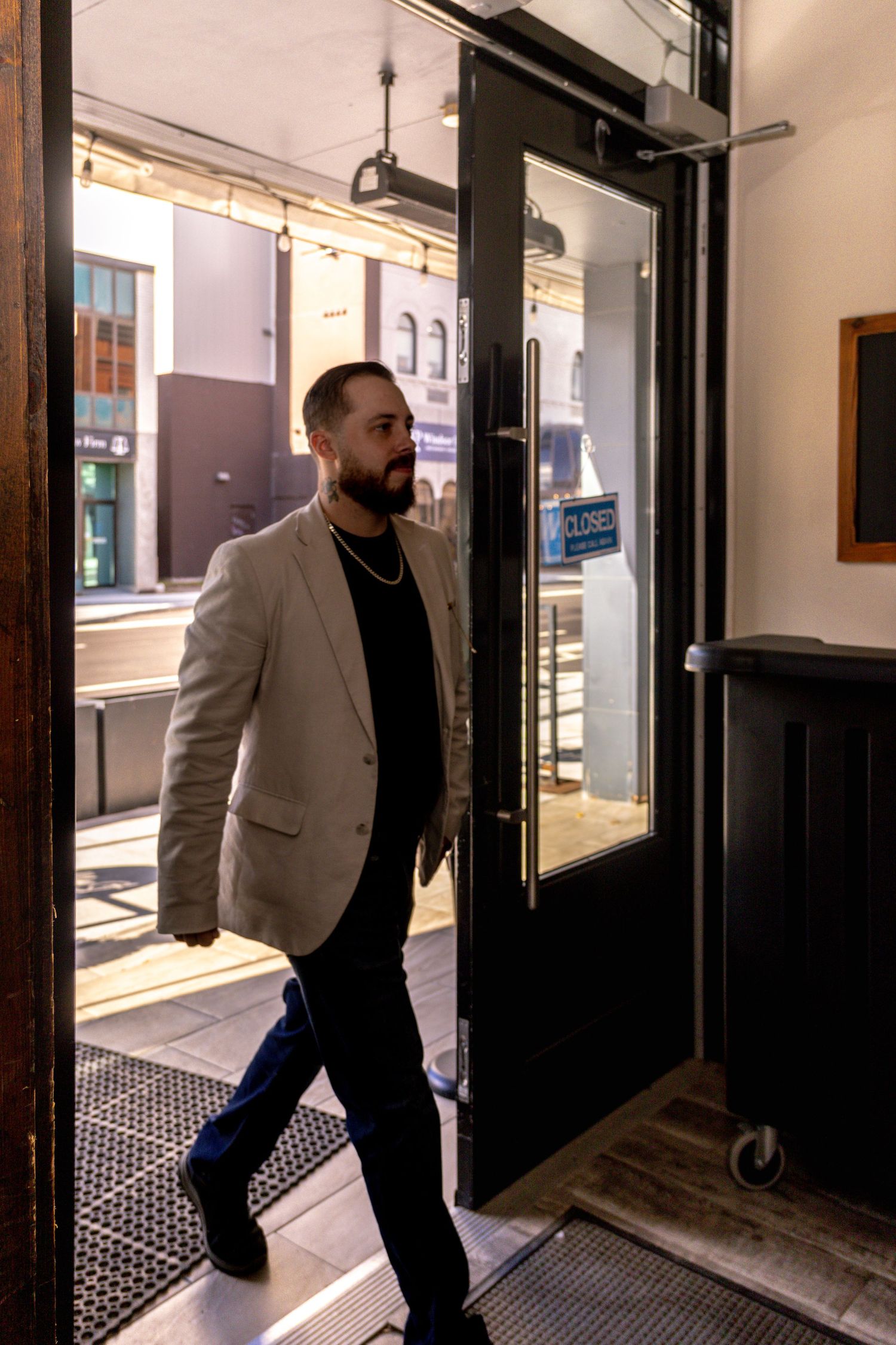 A person wearing a light blazer walks through a modern building entrance.