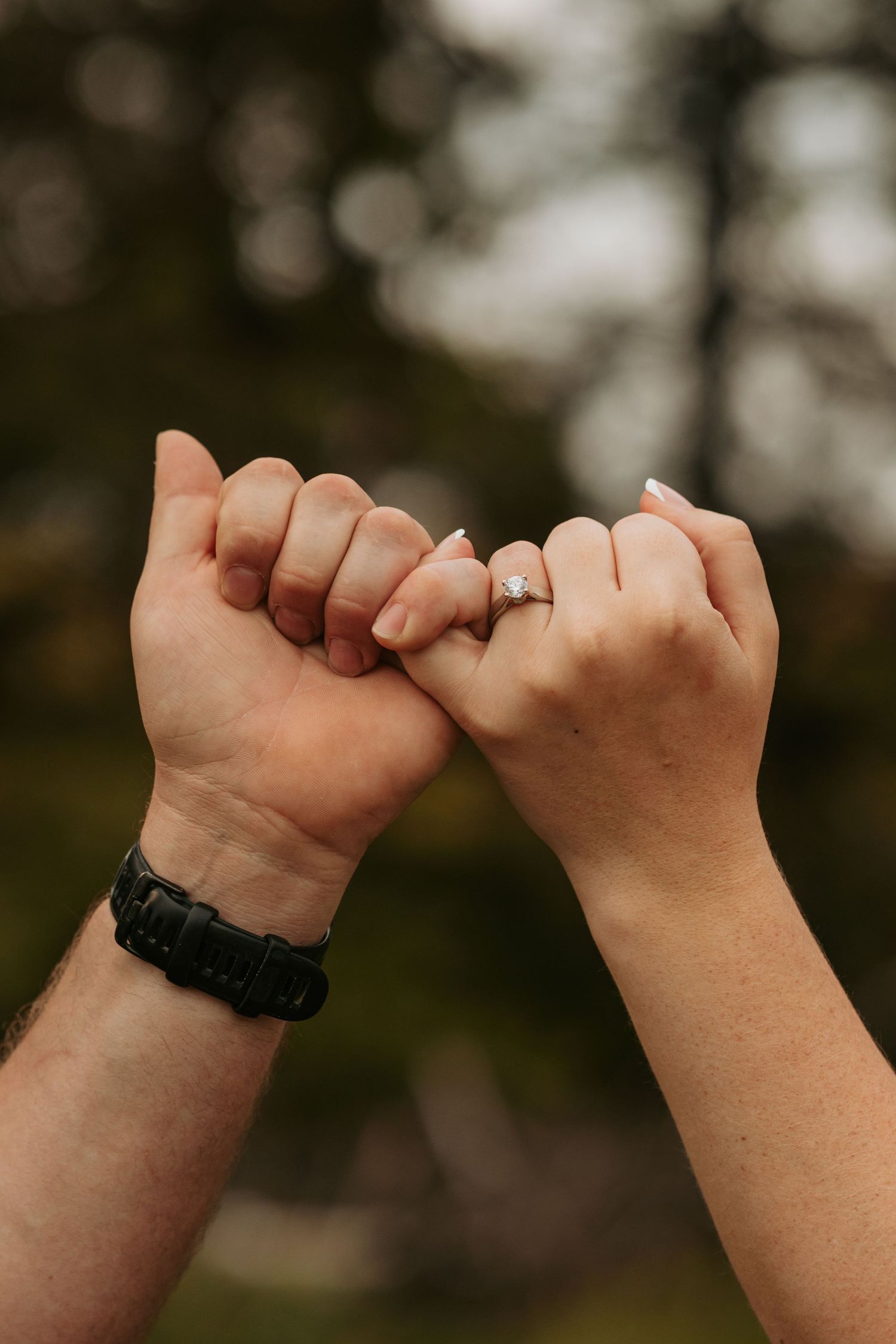 Close up of pinky promise hands against blurred natural background.