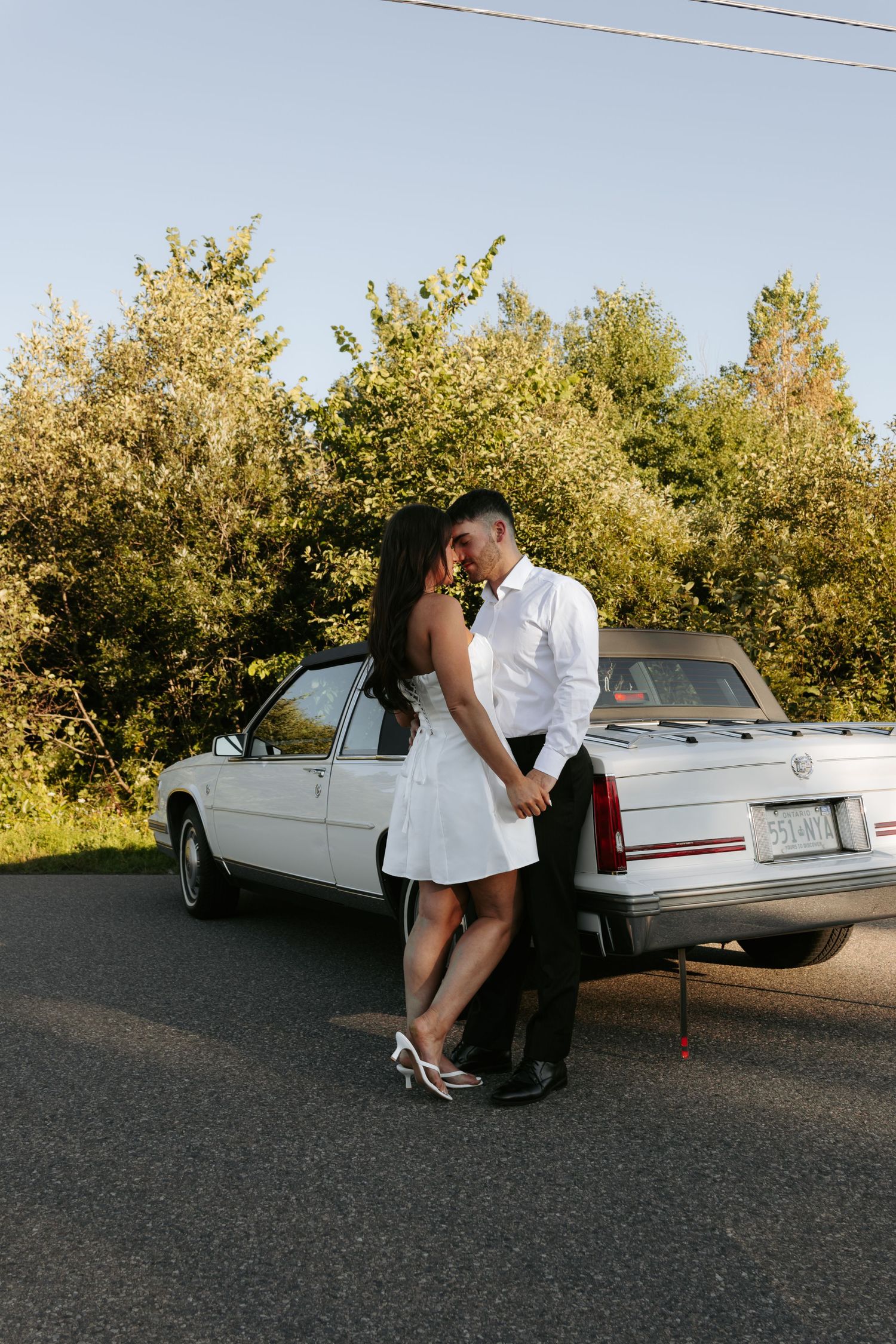 Romantic photoshoot with couple against white classic car at sunset.
