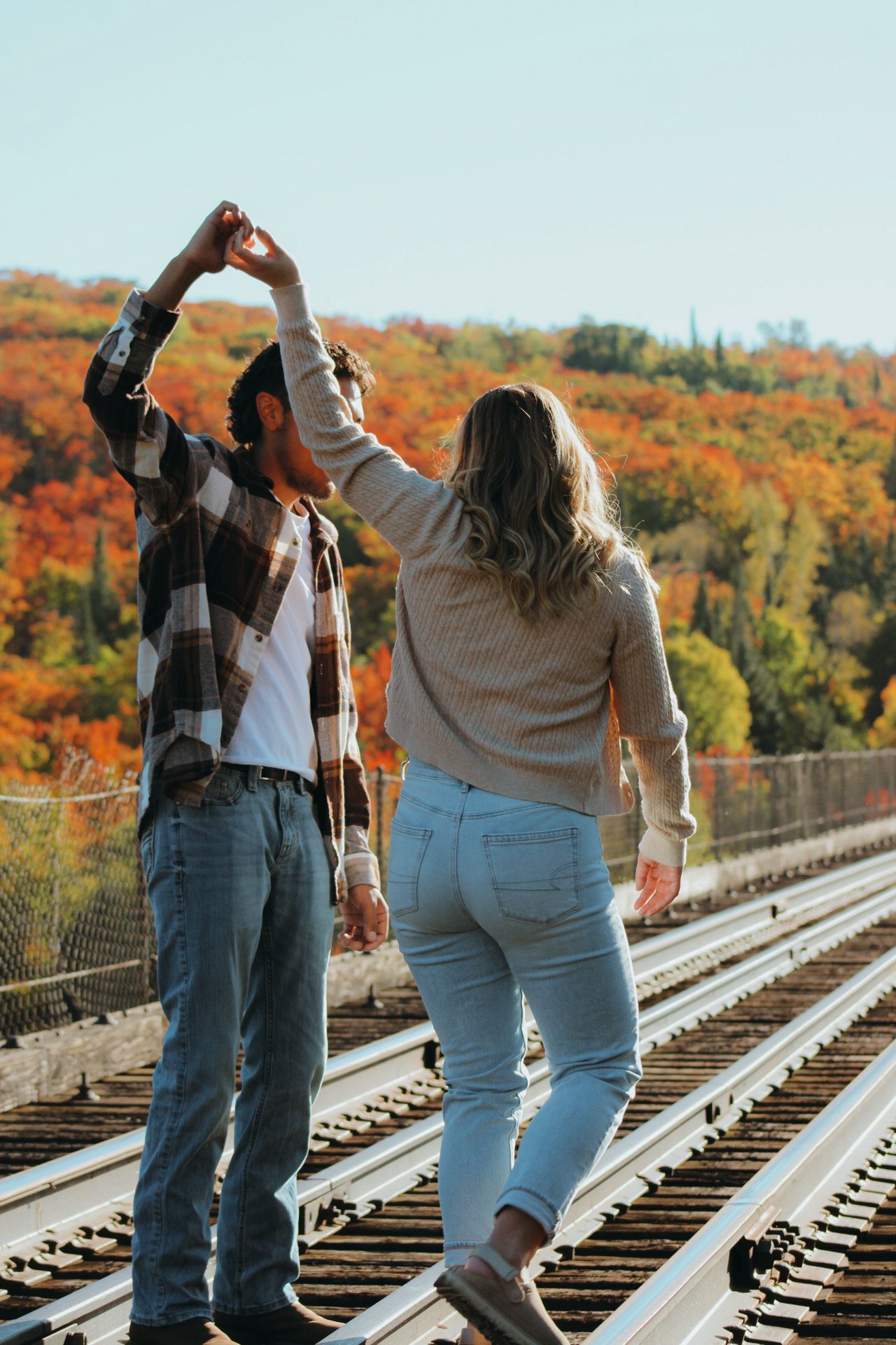 Dancing figures silhouetted against colorful fall trees on a railway bridge.