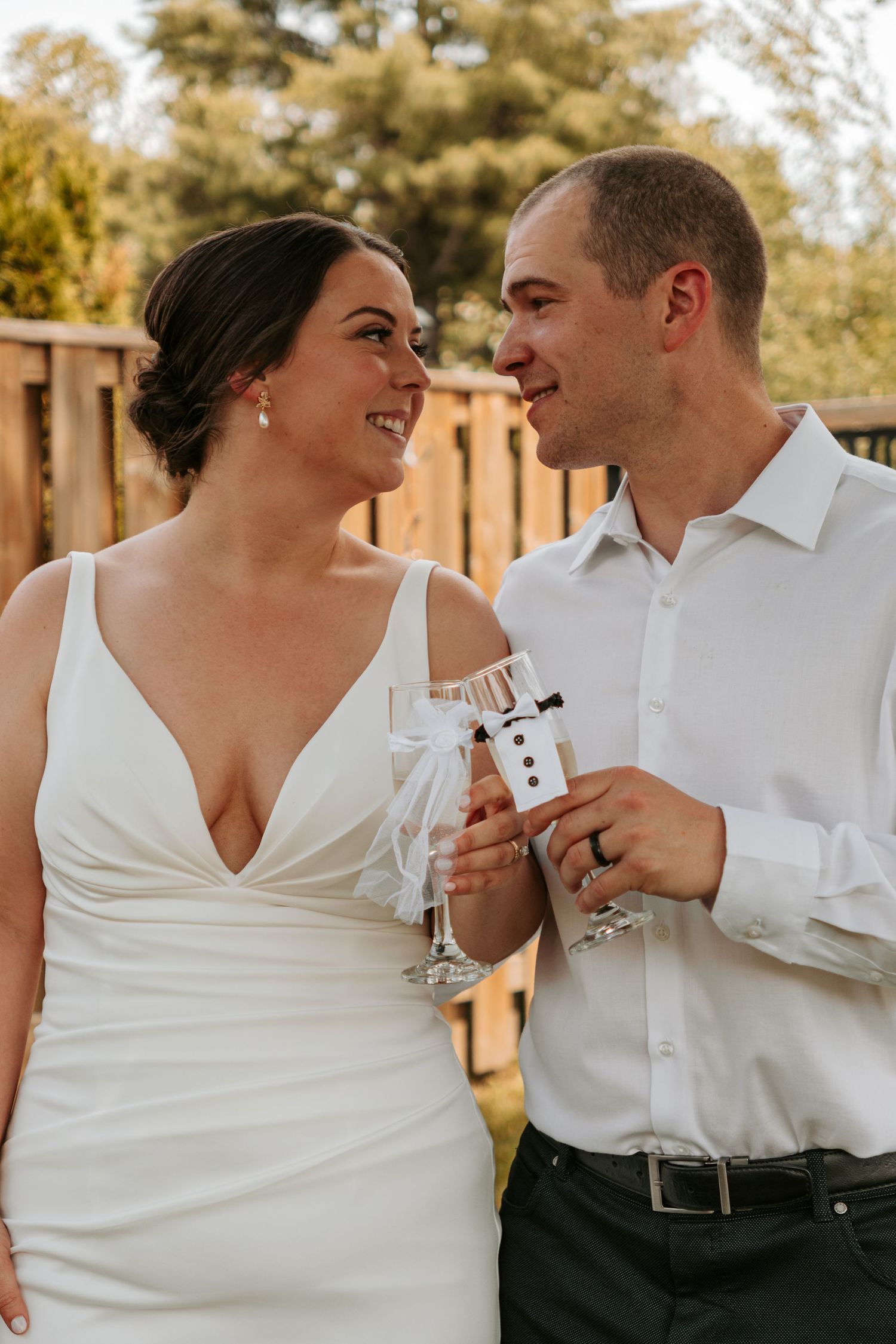 A couple in white wedding attire shares intimate moments while holding champagne glasses.