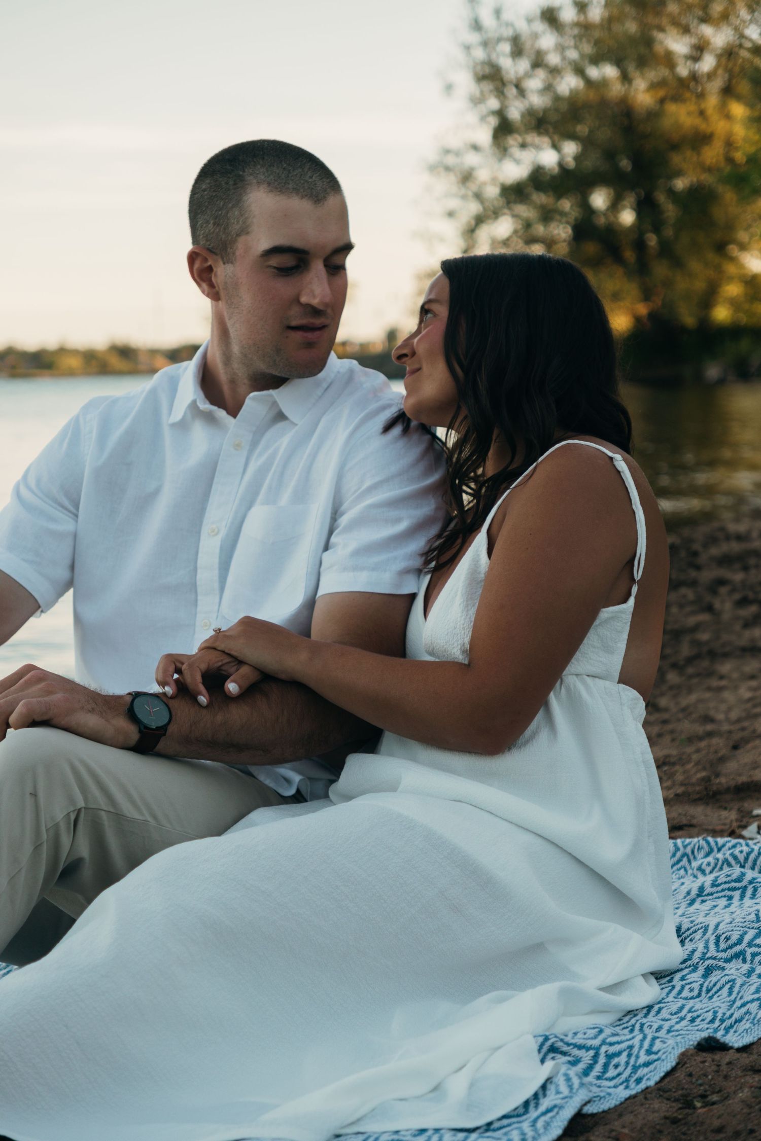 Romantic couple lounging on blue patterned blanket during outdoor photoshoot.