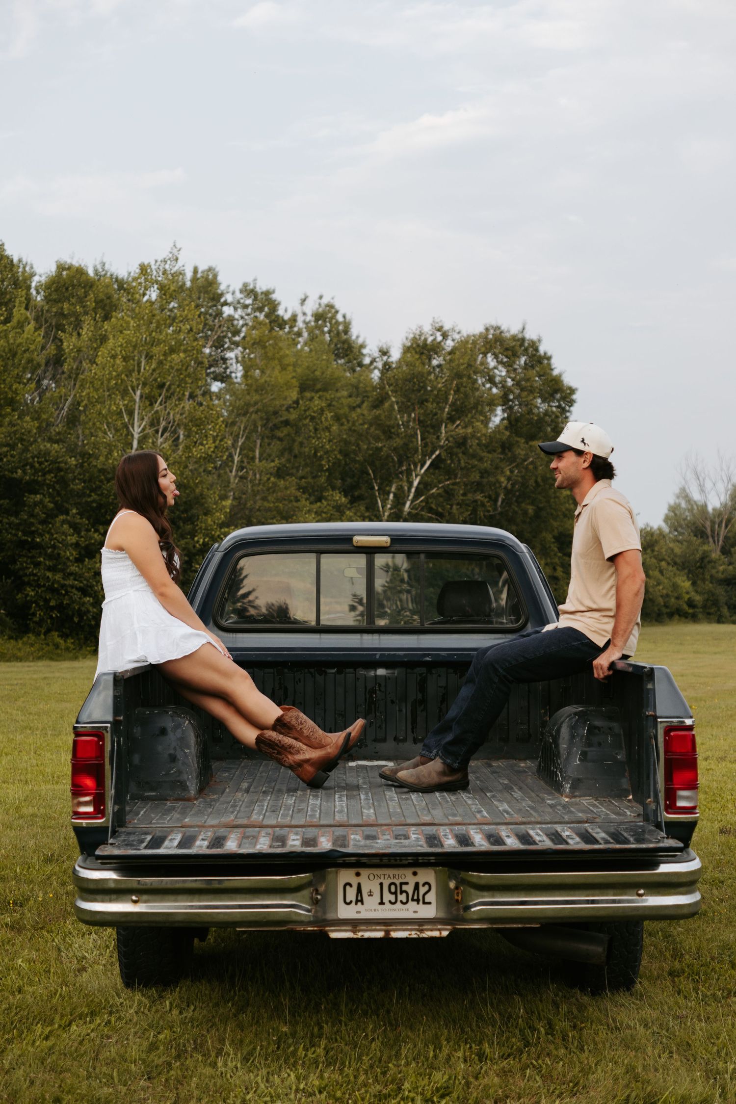 A couple sits in the bed of a vintage pickup truck in a rural field.