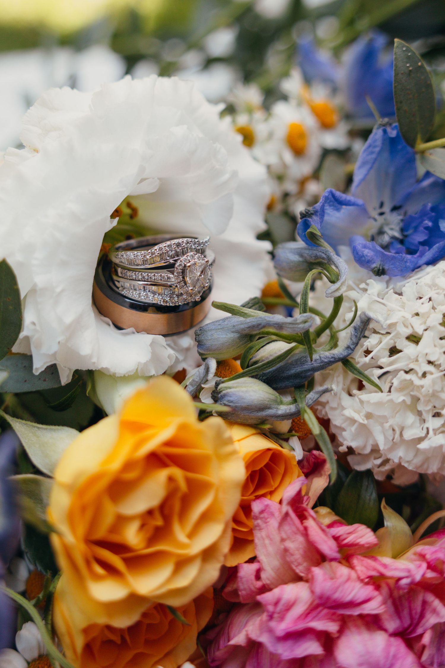 Wedding rings displayed on colorful flower arrangement with white and orange blooms.