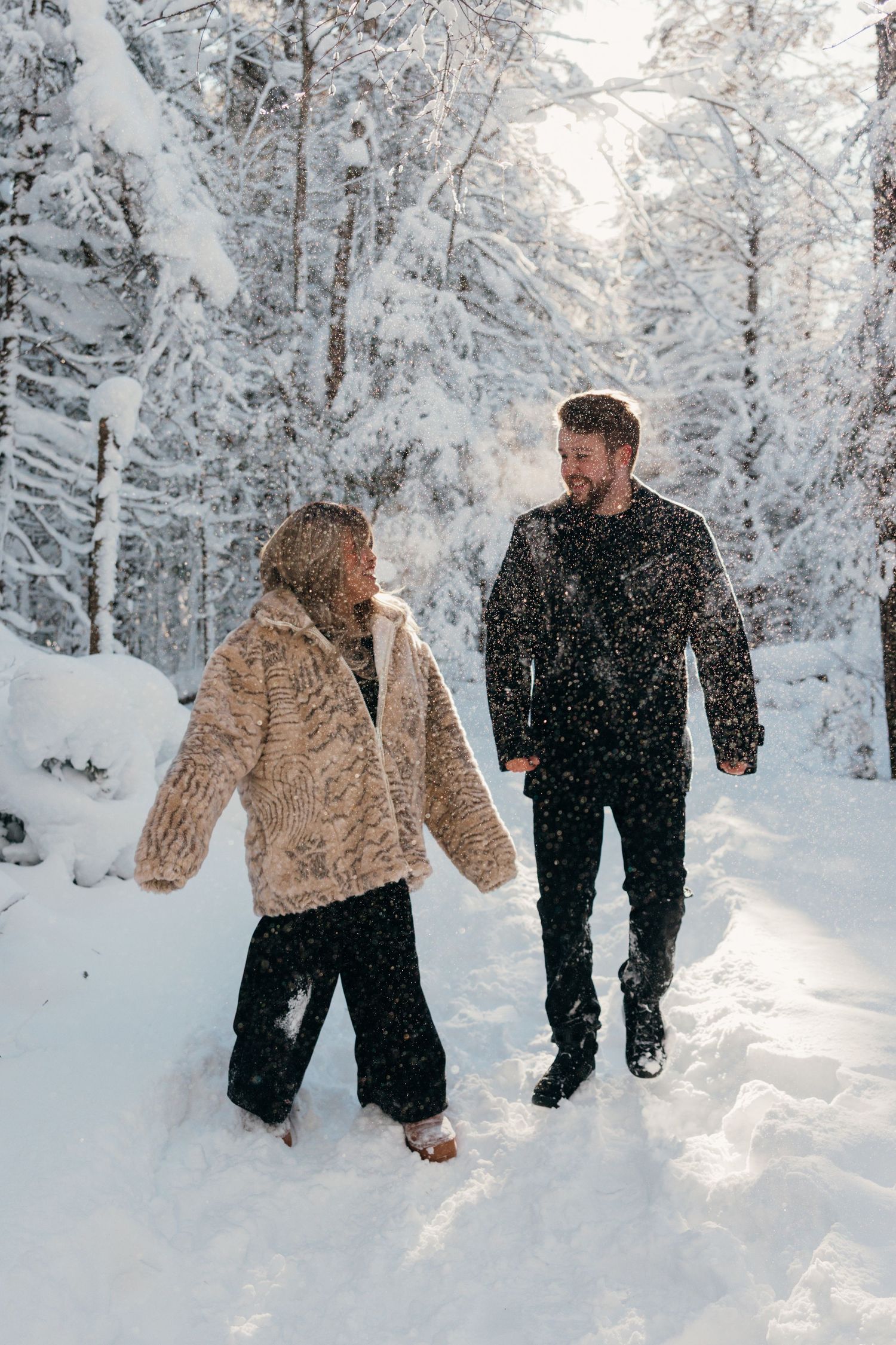 A couple playfully walks through deep snow in a winter wonderland forest setting.