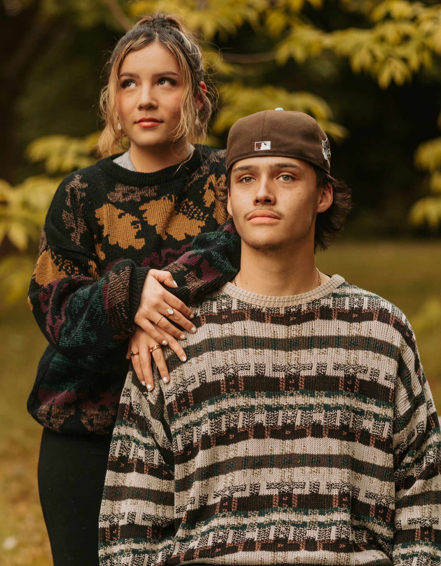 Couple in casual fall attire embracing outdoors with autumn foliage in background.