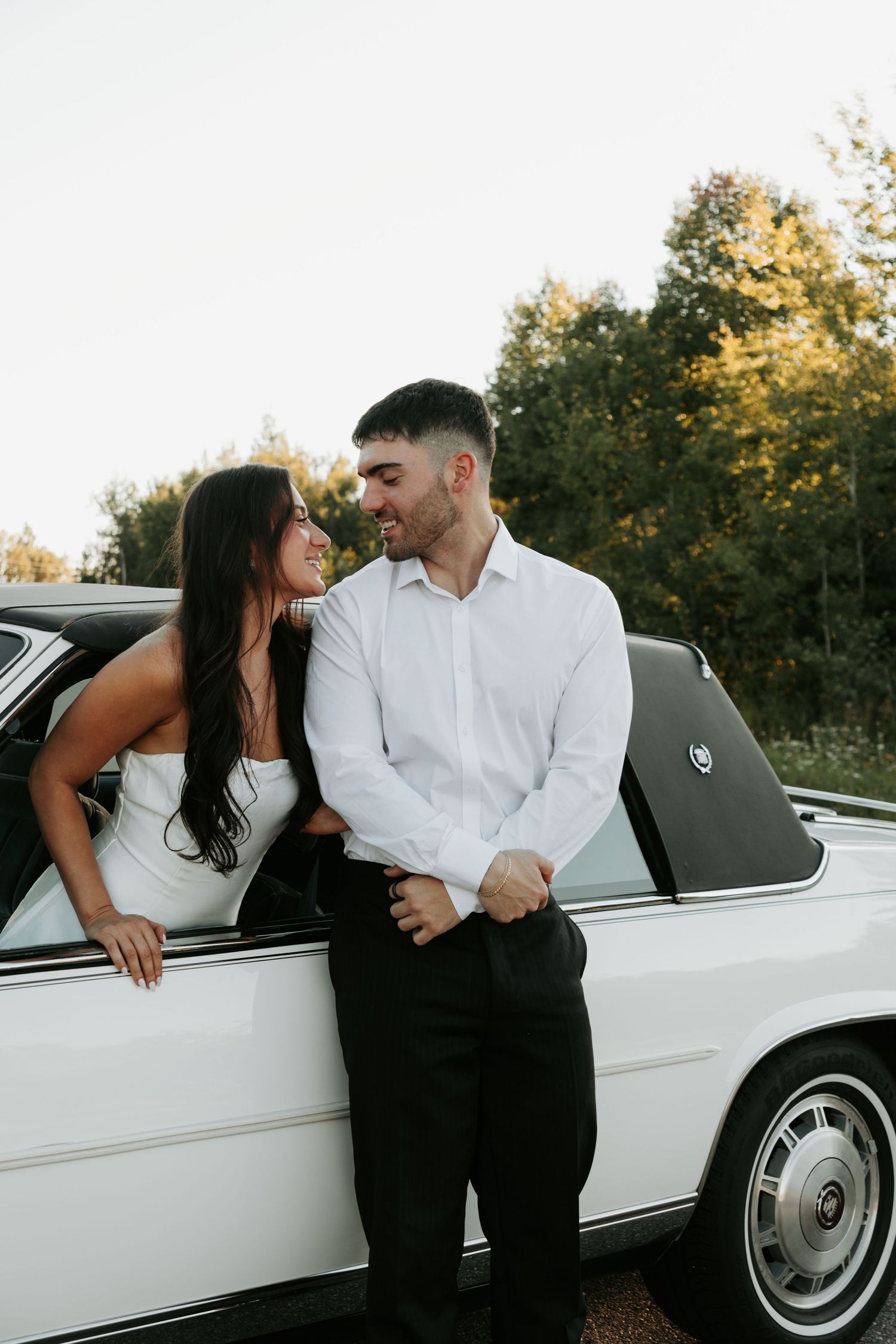 Couple dressed in contrasting black and white sharing tender moments beside a classic car.