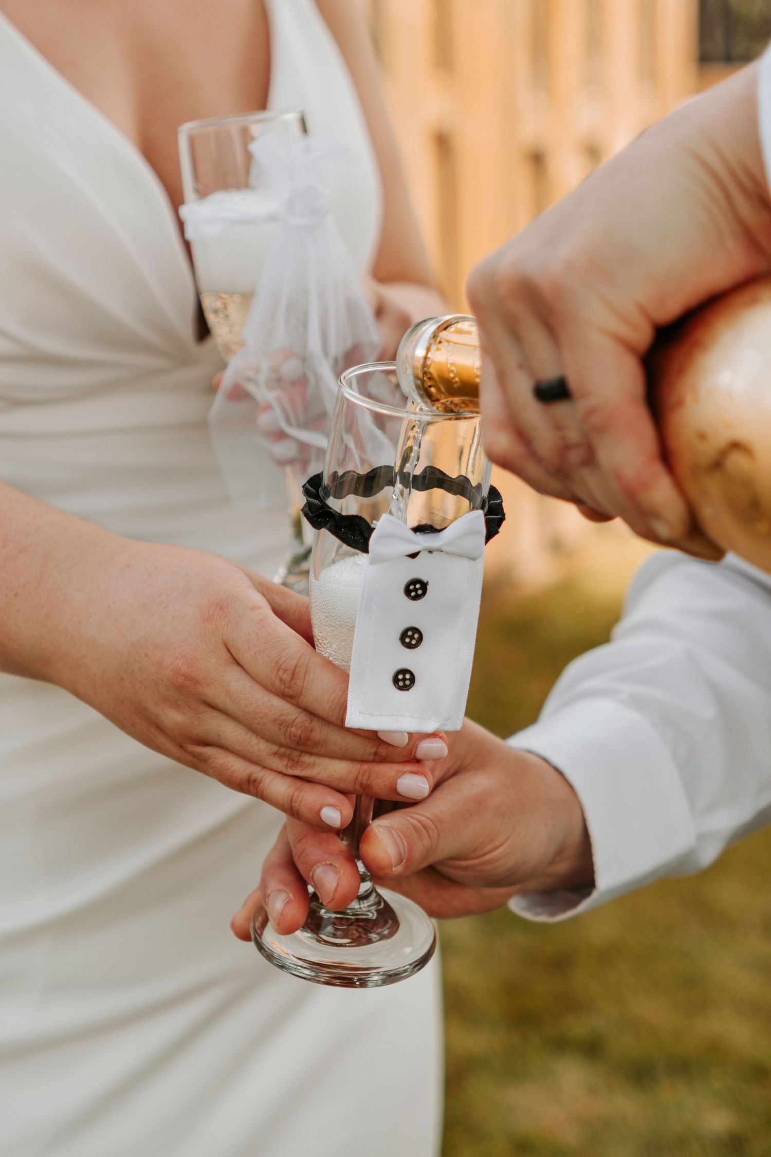 Close-up of hands holding decorated wedding champagne glasses with tuxedo-styled ornaments.