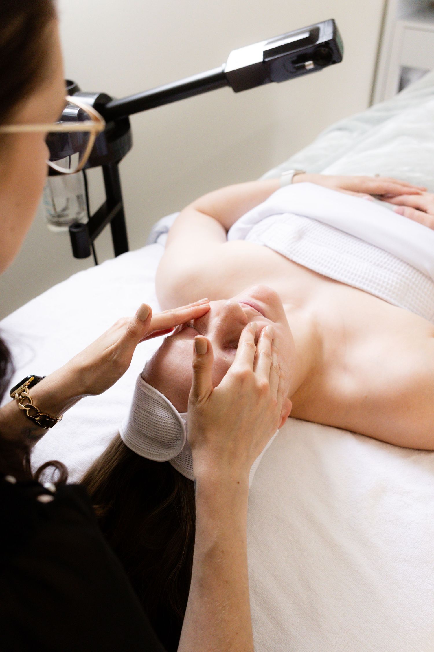 Esthetician performing a professional facial treatment on a client lying on a spa treatment bed.