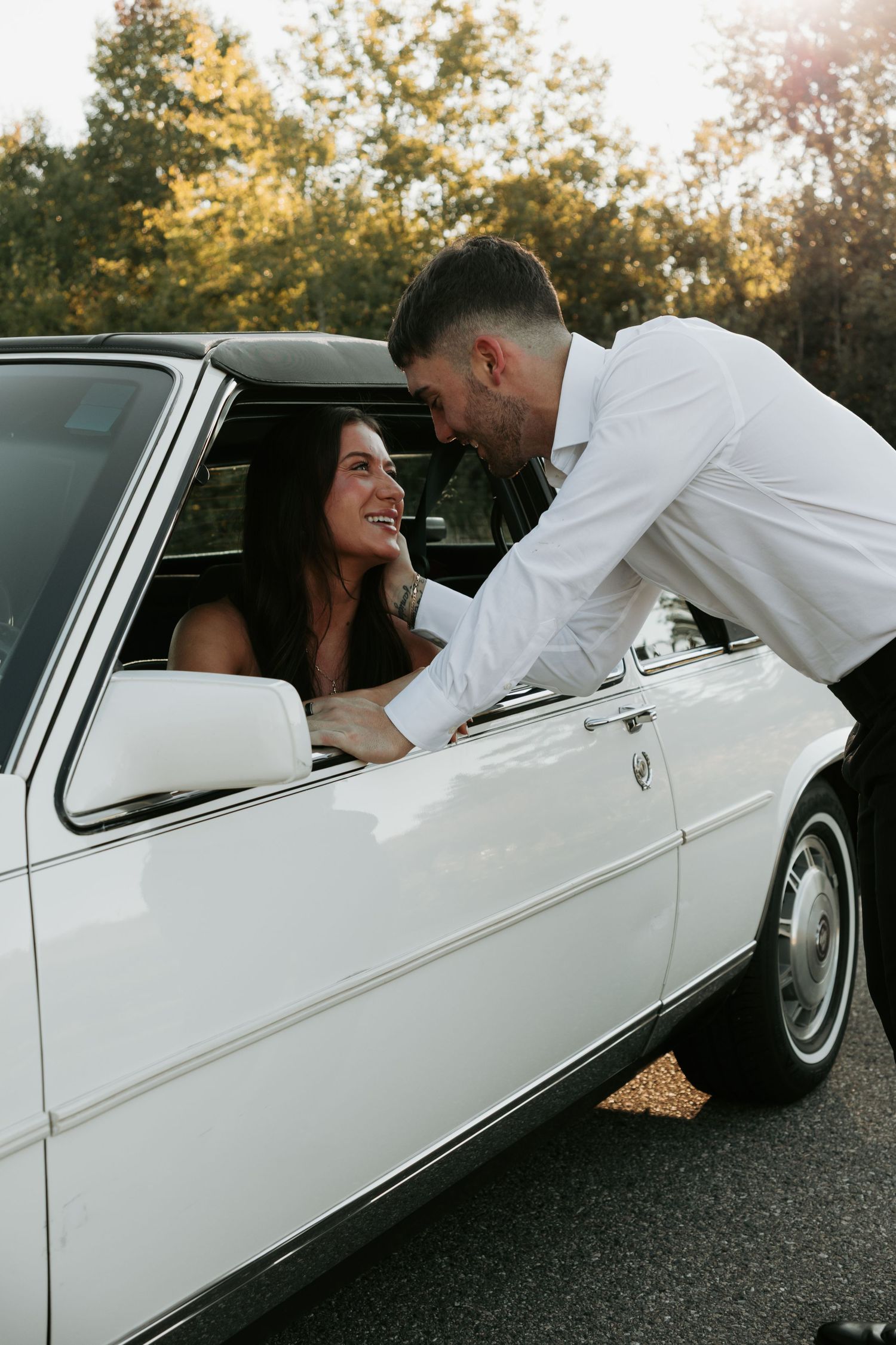 Couple leans into classic white car for romantic sunset portrait.