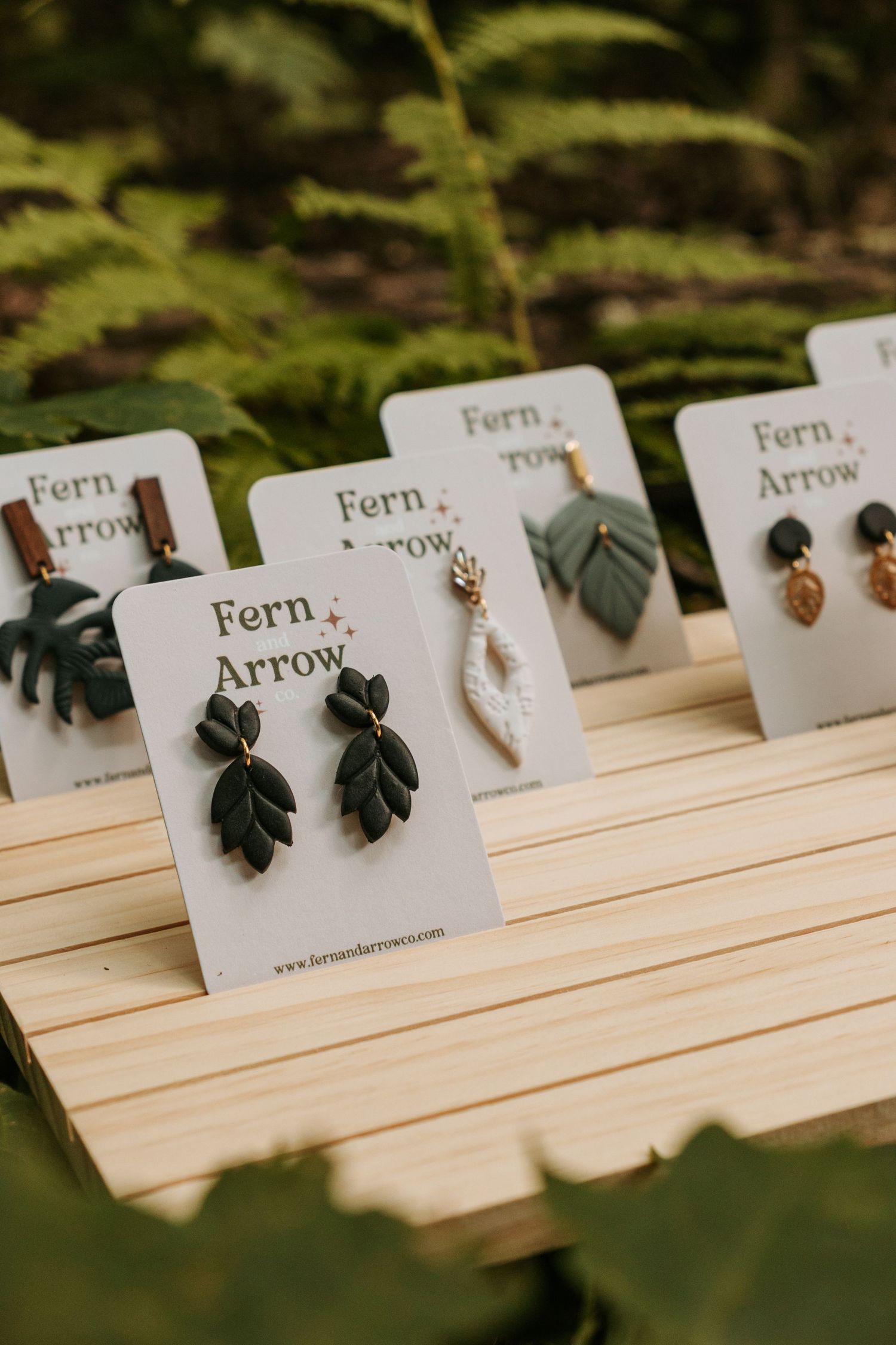 Display of Fern & Arrow leaf-shaped earrings on wooden display cards.
