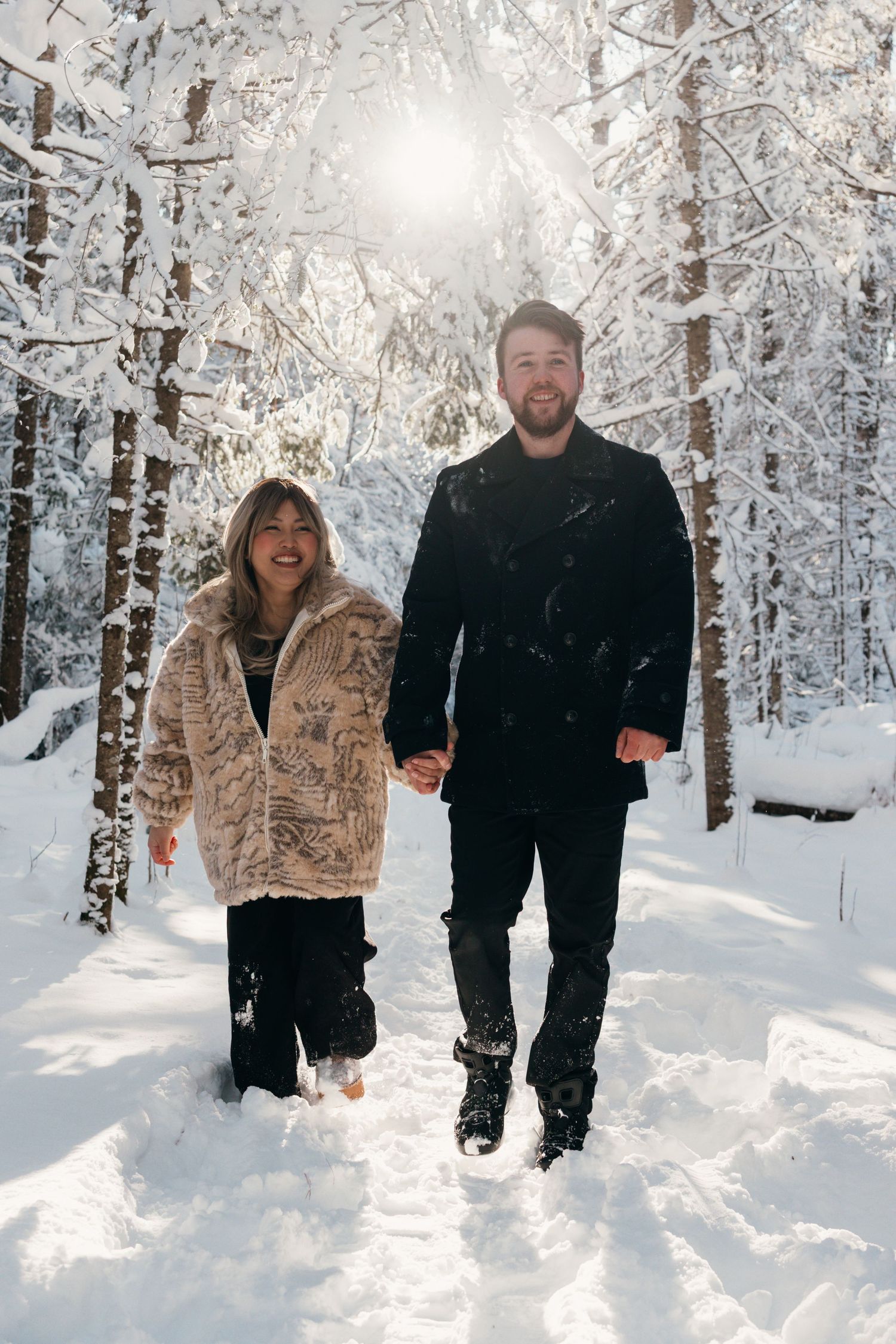 A couple walks through a snowy winter forest with snow-covered trees creating a magical white landscape.