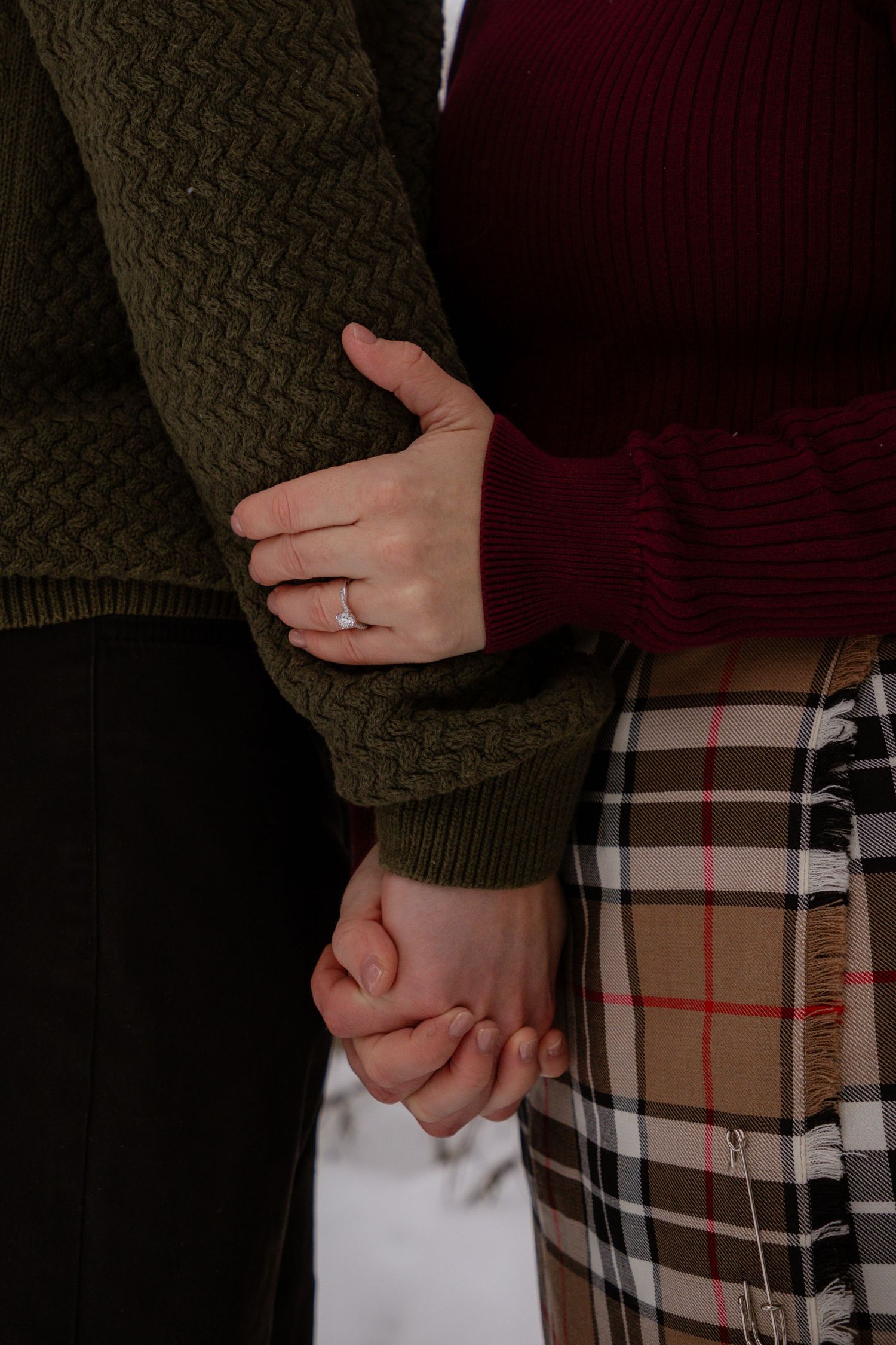 Close-up detail shot of hands with an engagement ring against plaid fabric in winter.
