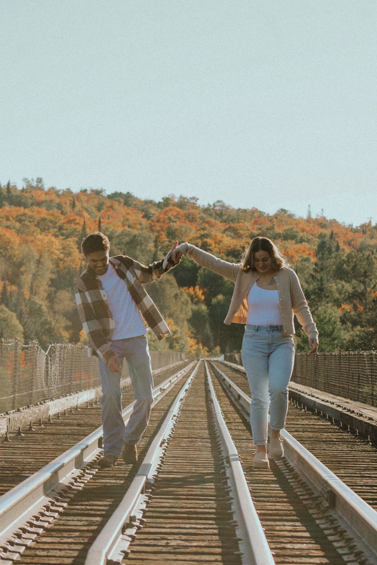 Couple dancing and twirling on railroad tracks with autumn foliage backdrop.